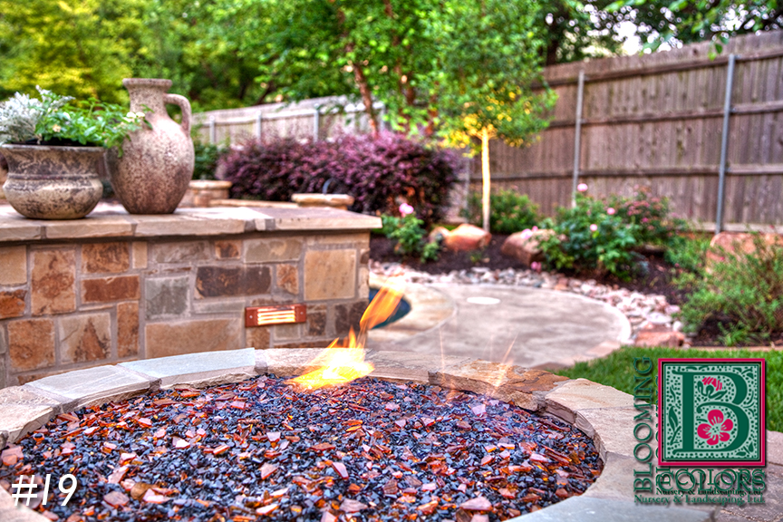 Gas fire pit with glass stones and stone wall landscaping in Colleyville, TX