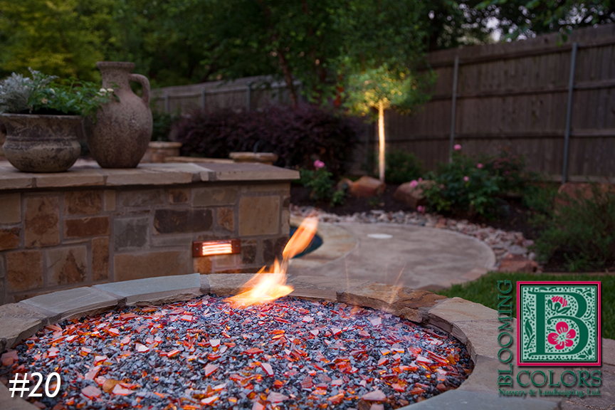 Backyard fire pit with flames, flagstone and stone planter wall at dusk