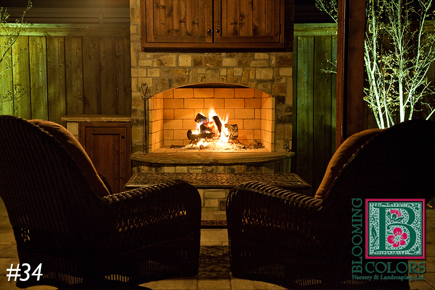 Wicker armchairs facing a lit stone fireplace on a patio at night