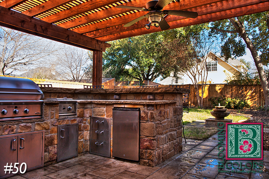 Pergola-covered outdoor kitchen with stainless grill and stone counter