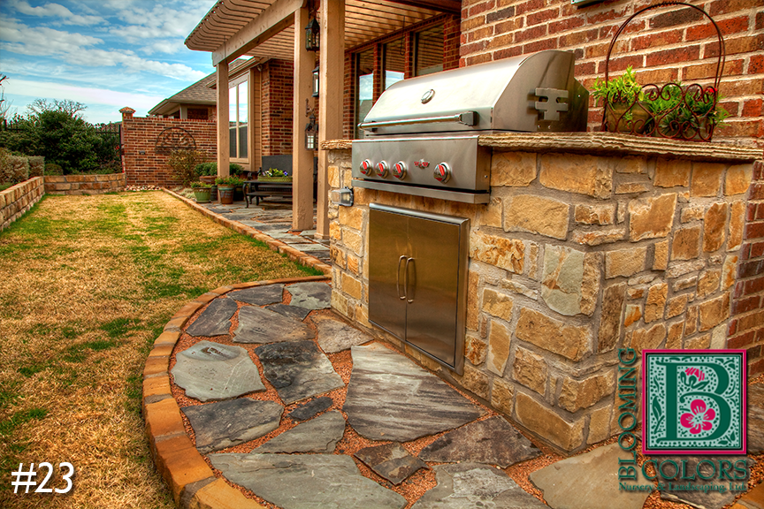 Stone outdoor grill station on a flagstone path beside a brick home