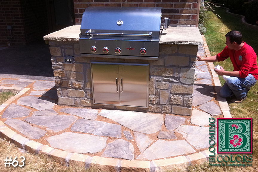 Stone outdoor grill built into a flagstone patio as a homeowner kneels beside it