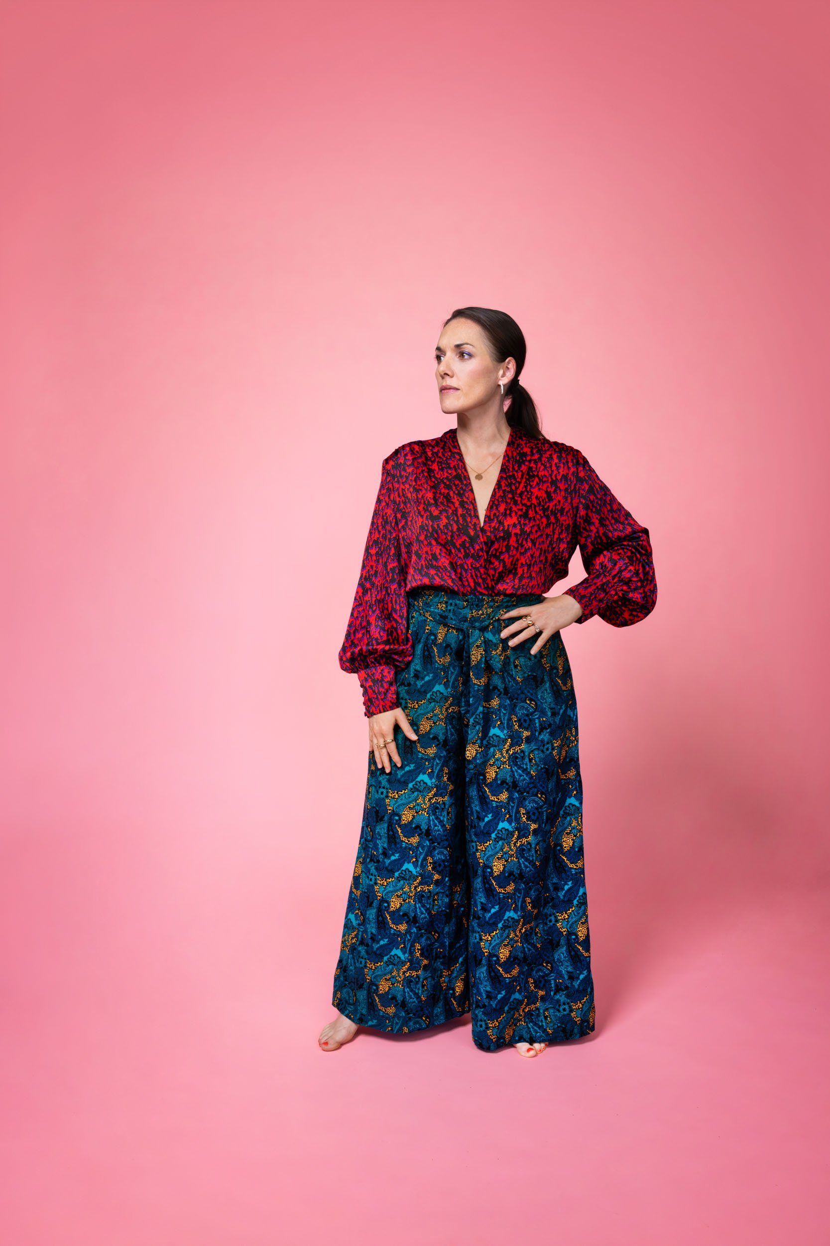 Maria Finkelmeier standing up with one hand on her hip, on a pink background