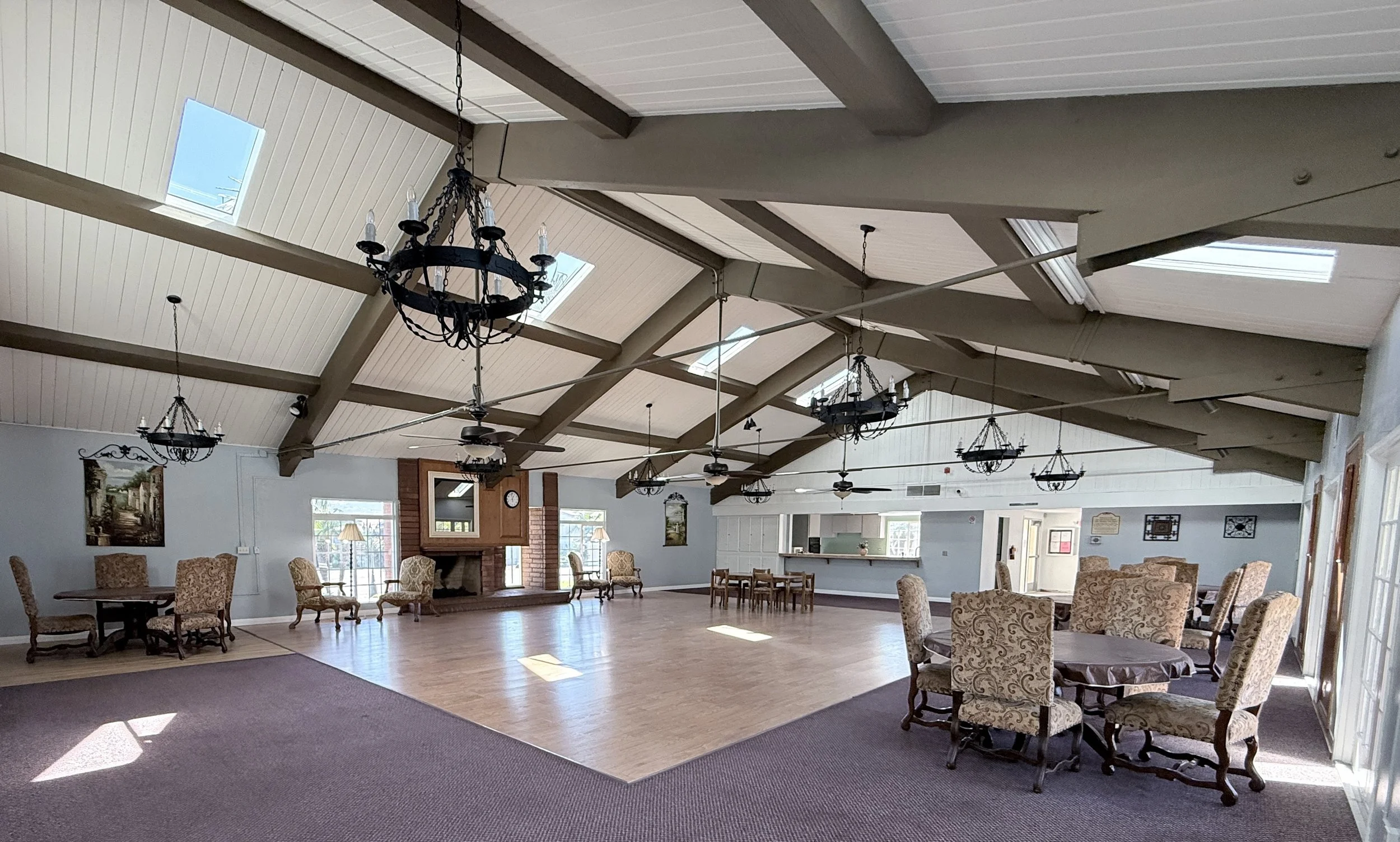 Clubhouse hall with a vaulted beamed ceiling, chandeliers, a brick fireplace and a wood dance floor.