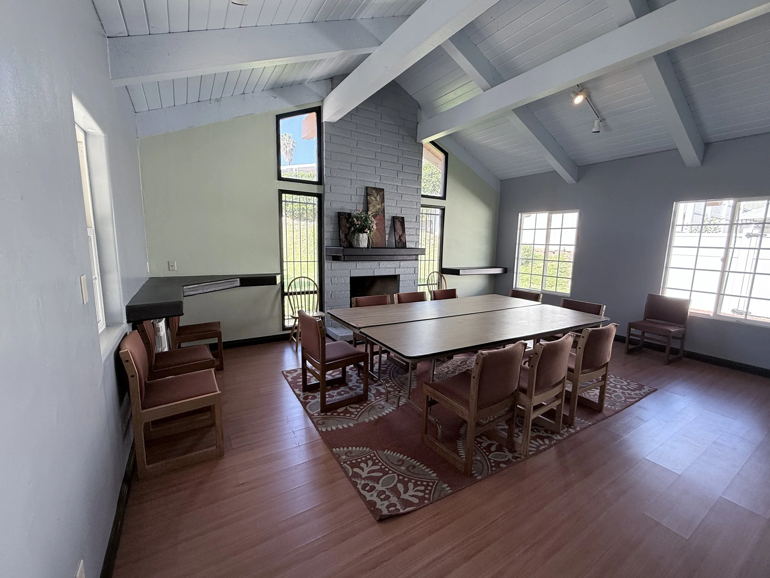Meeting room with a painted brick fireplace, long tables and chairs, and tall windows.