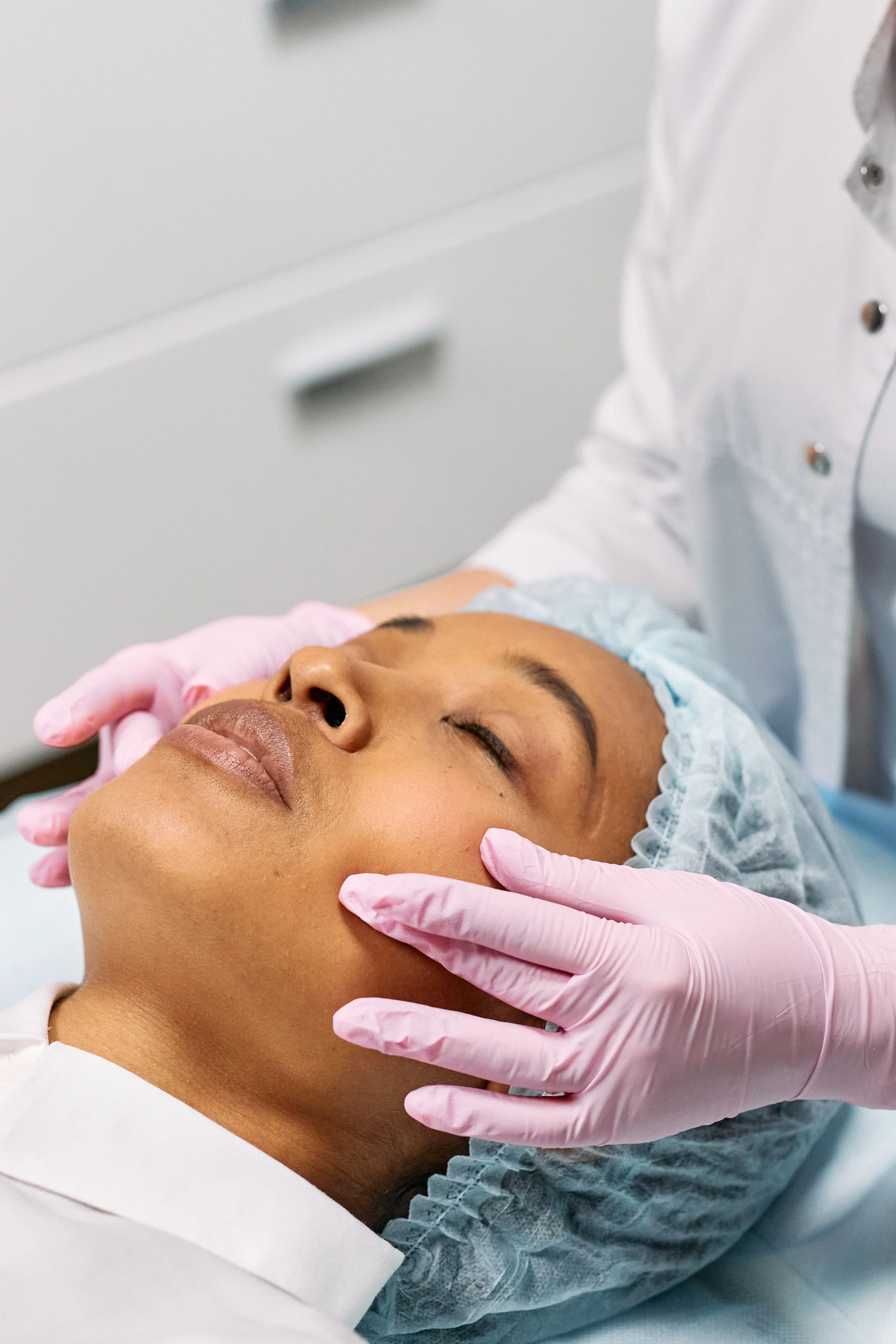 Healthcare professional in pink gloves examining a newborn baby’s face