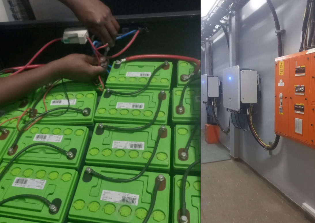 Technician wiring green battery cells beside an industrial battery backup system and orange electrical control cabinet.