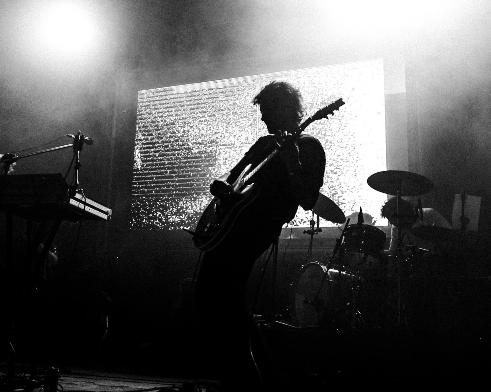 Guitarrista en silueta frente a una pantalla, en blanco y negro.