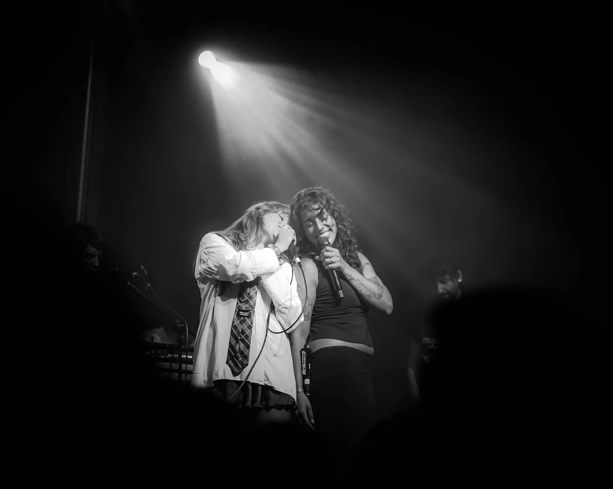Dos artistas compartiendo el escenario bajo un reflector, en blanco y negro.