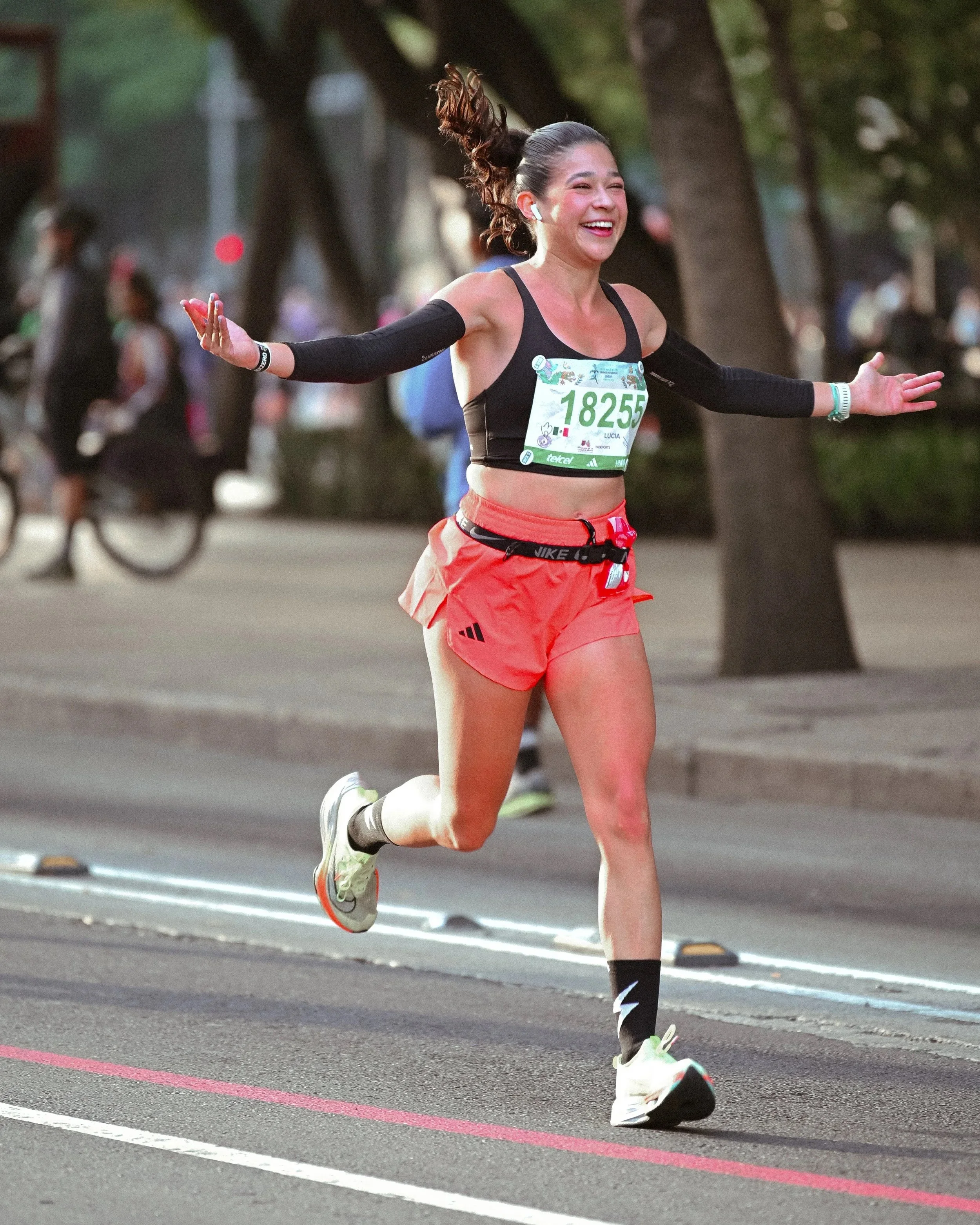 Corredora de shorts rojos sonriendo con los brazos abiertos durante una carrera.