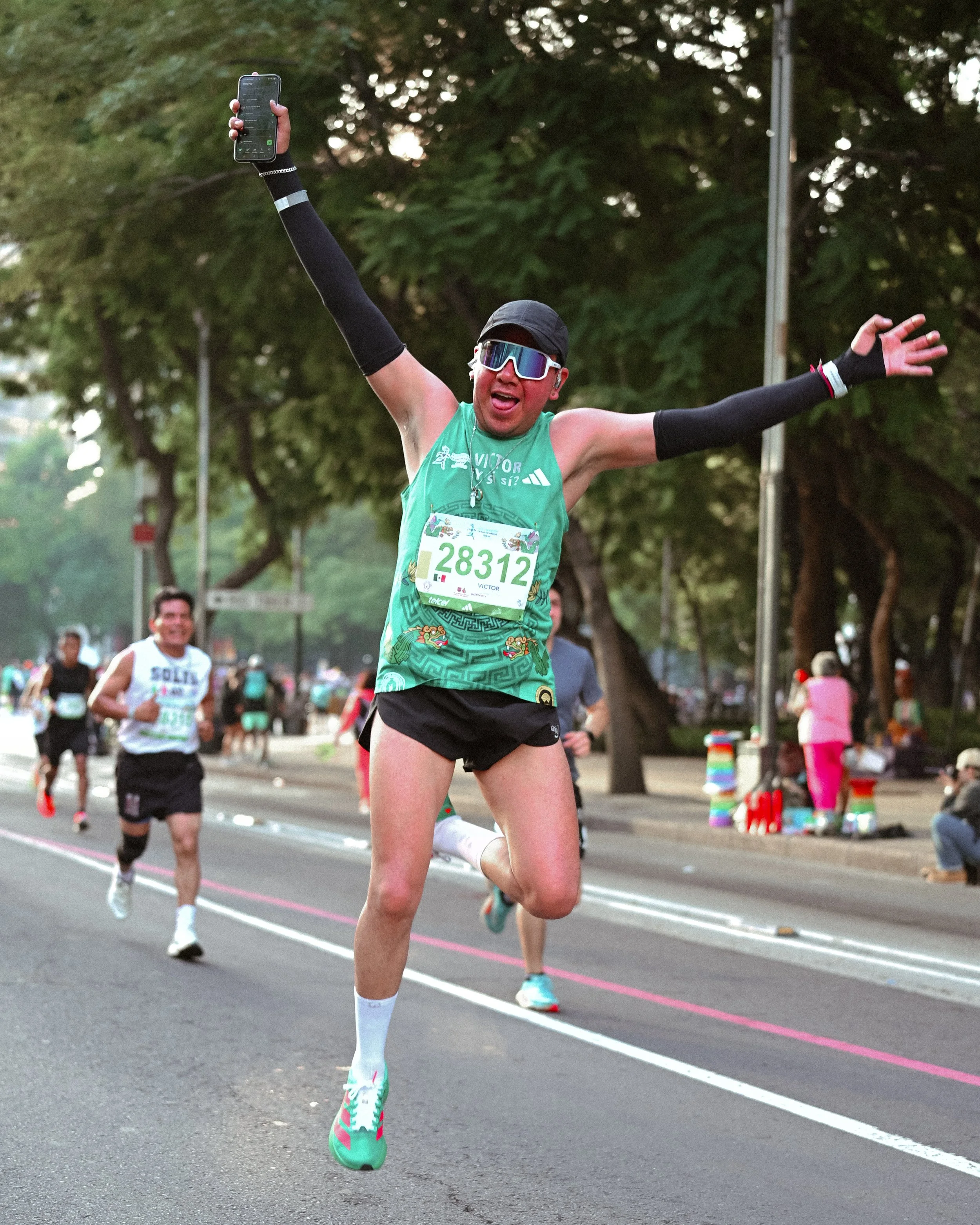 Corredora de camiseta verde levantando ambos brazos en la ruta.