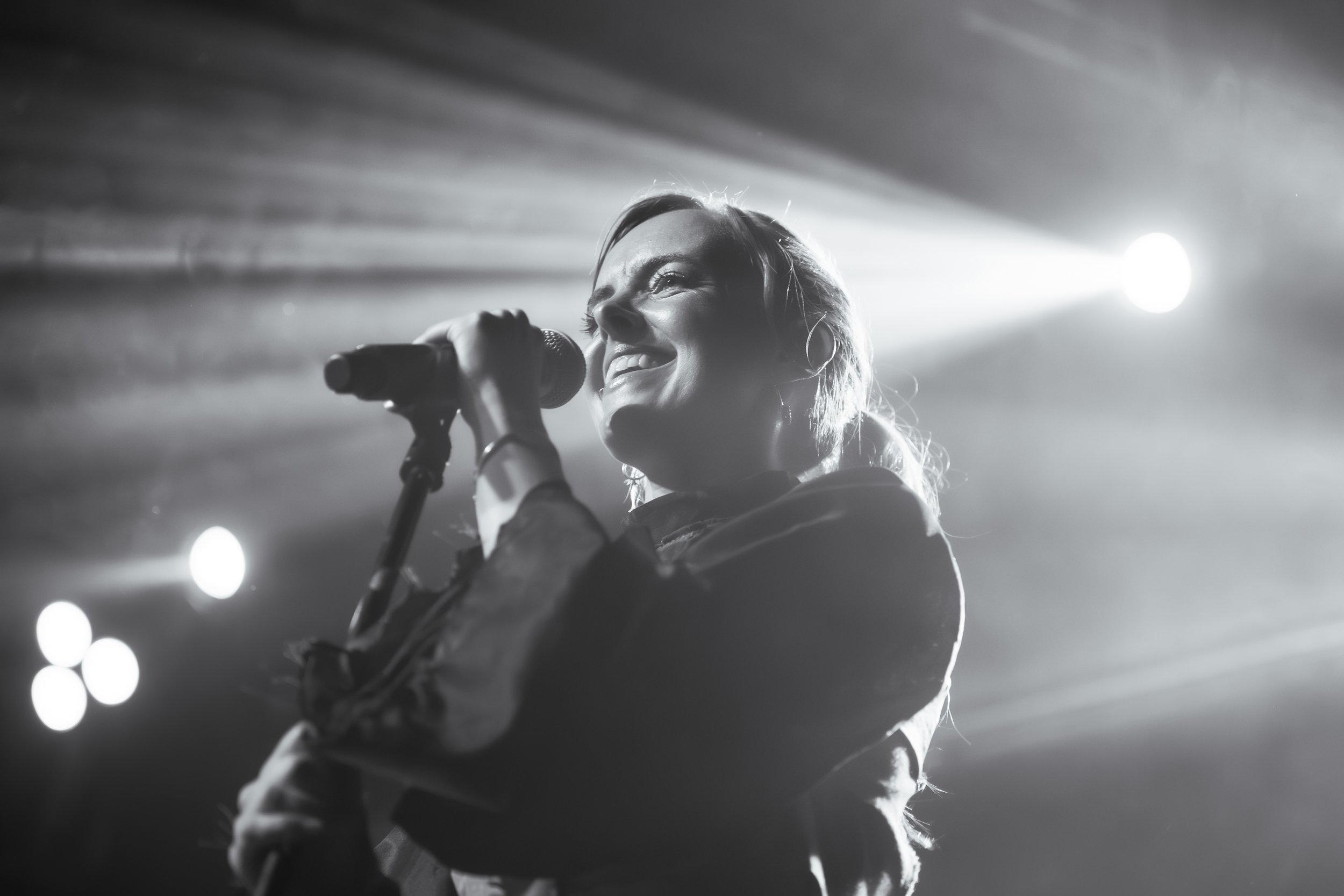 Cantante sonriendo frente al micrófono bajo un contraluz, en blanco y negro.