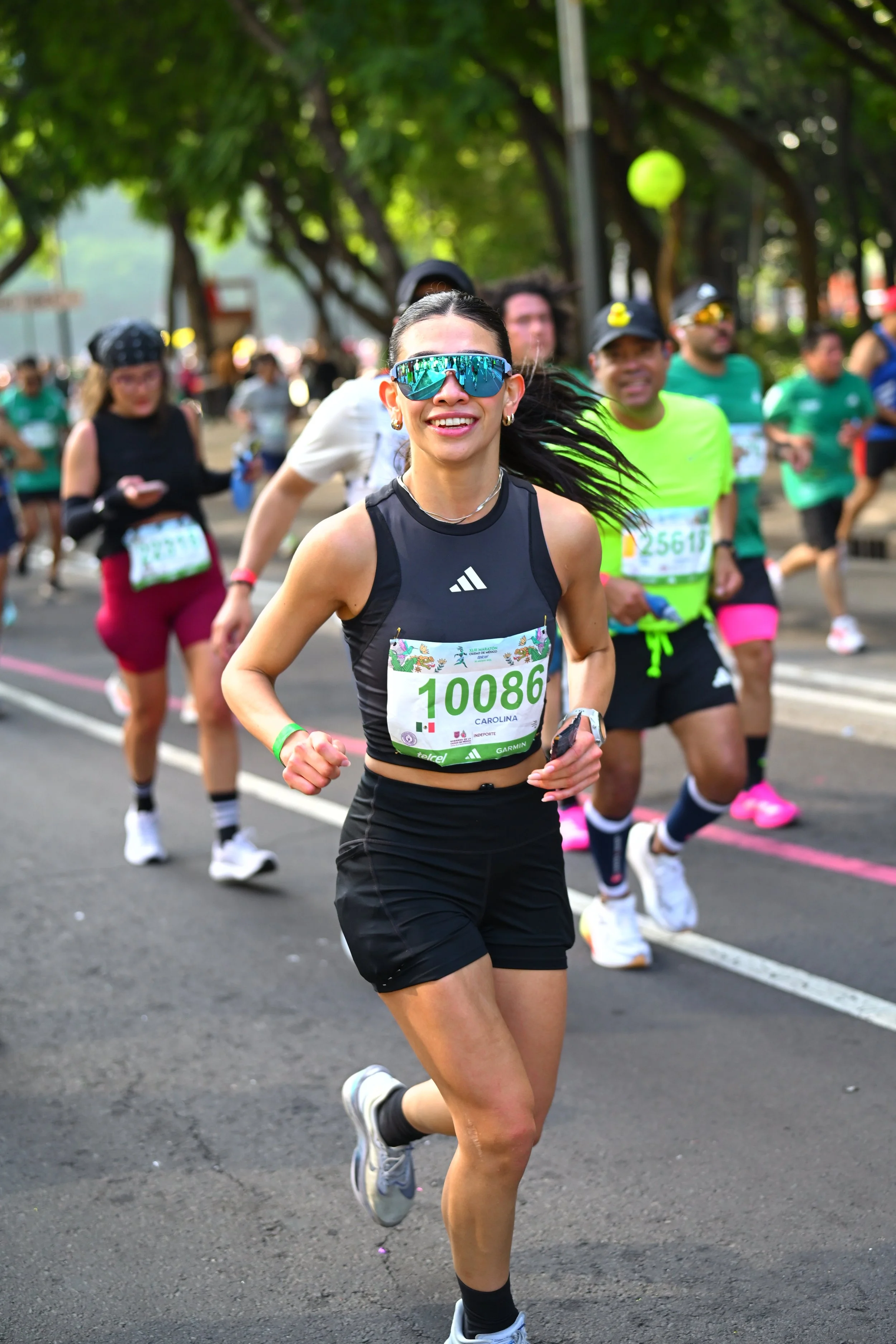 Corredora de camiseta negra y lentes reflejantes sonriendo durante la carrera.