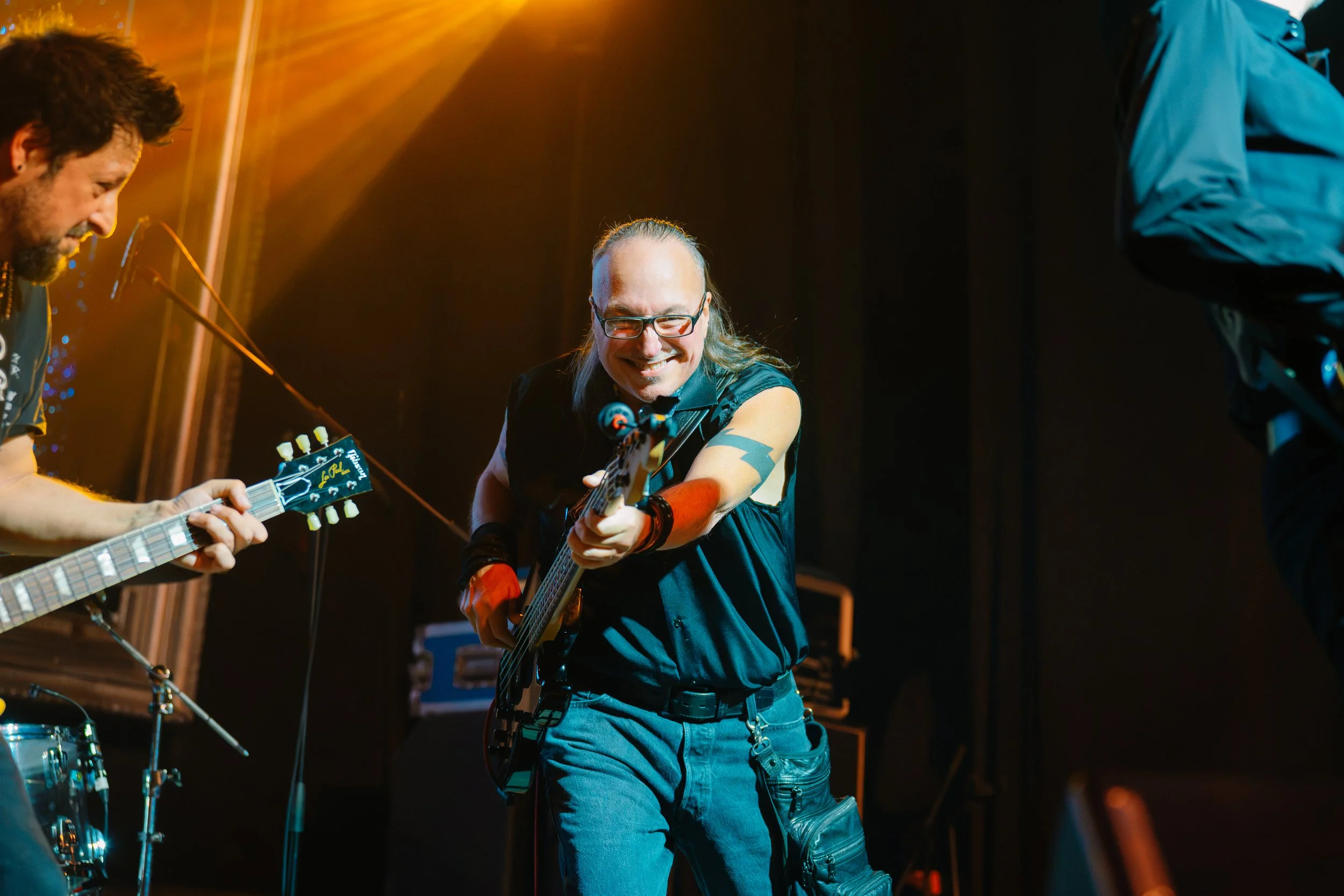 Guitarrista sonriendo mientras toca bajo una luz cálida.