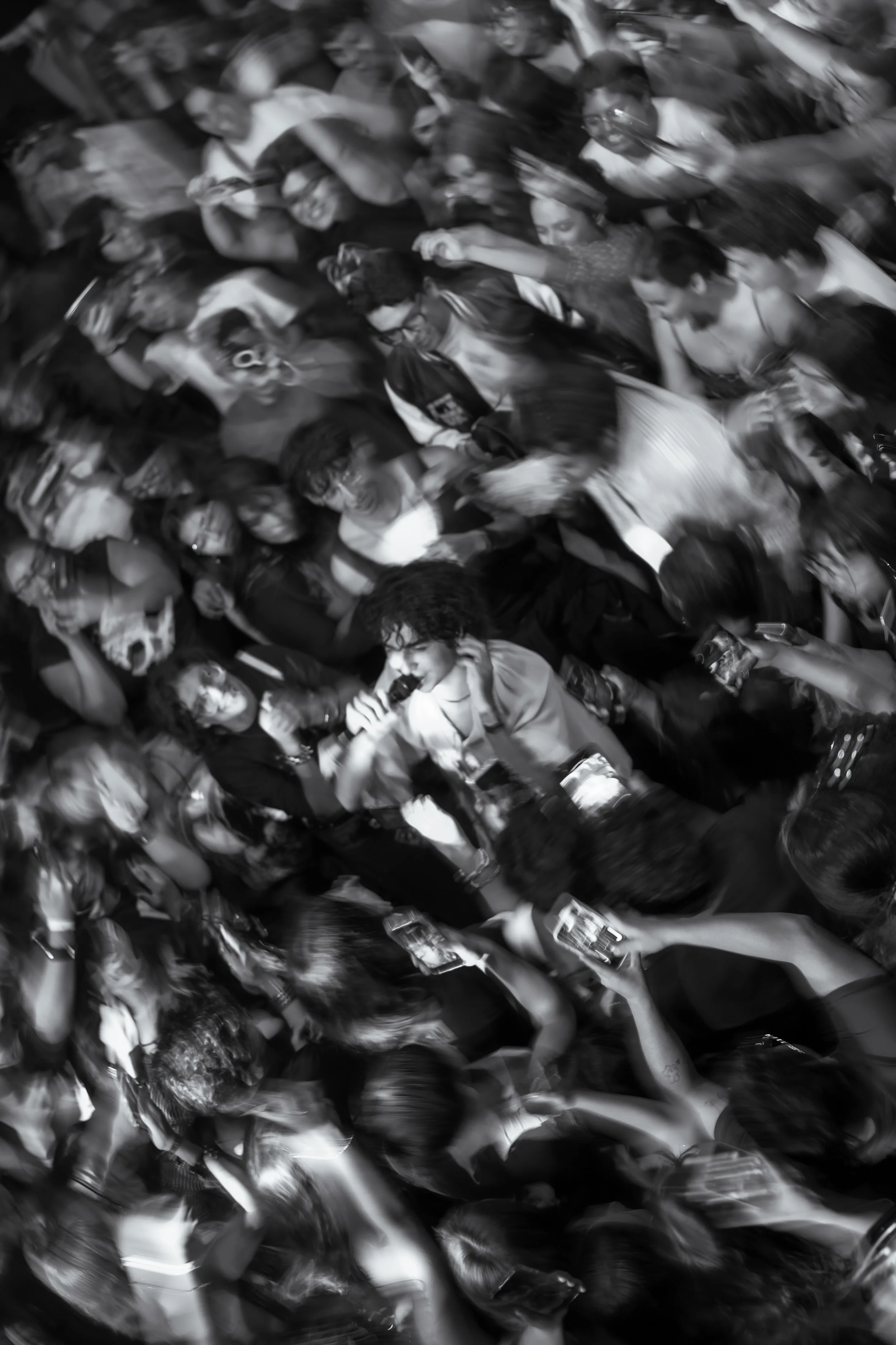 Público en movimiento durante un concierto, con efecto de barrido en blanco y negro.
