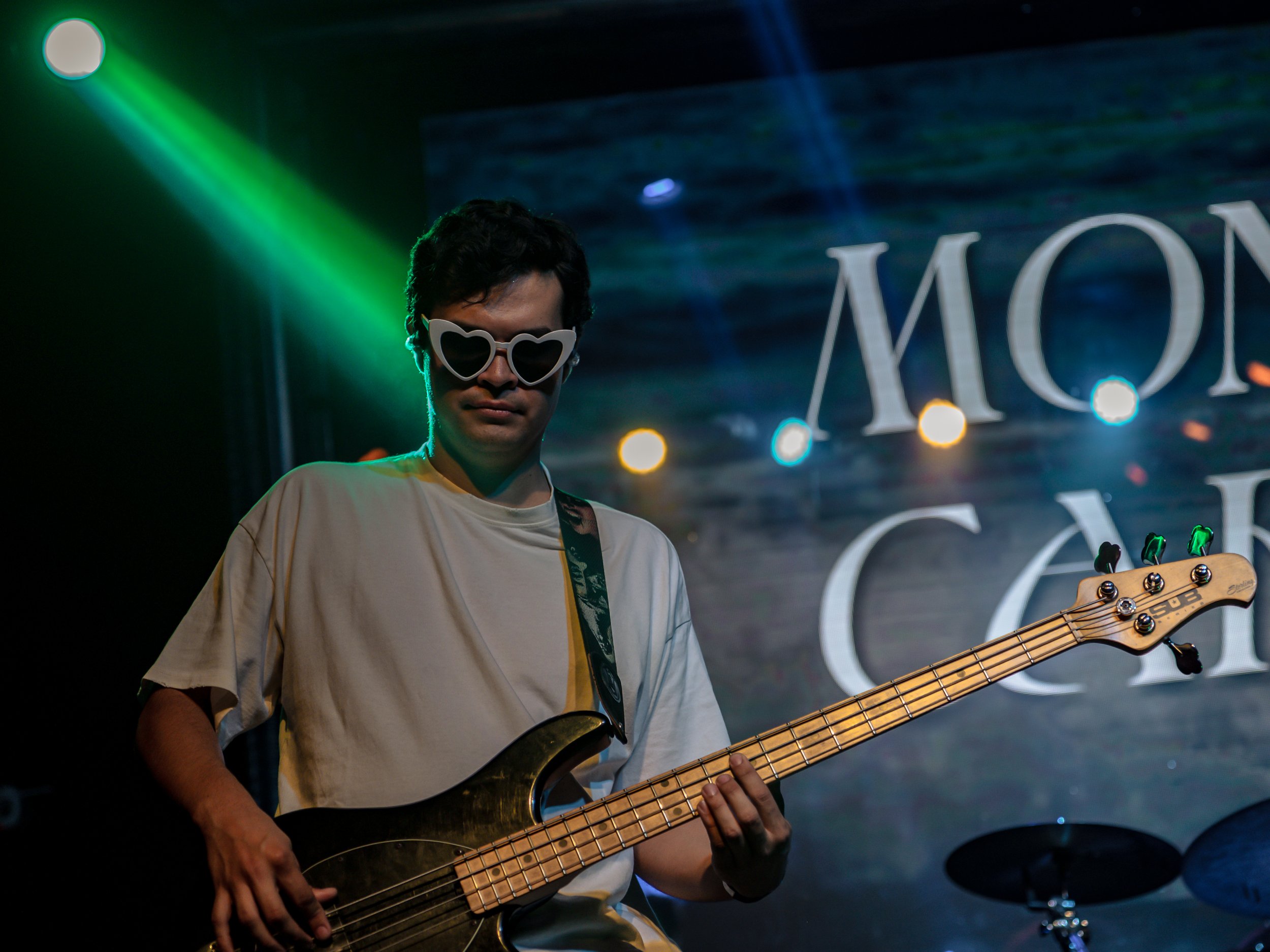 Bajista con lentes oscuros tocando bajo luces verdes.