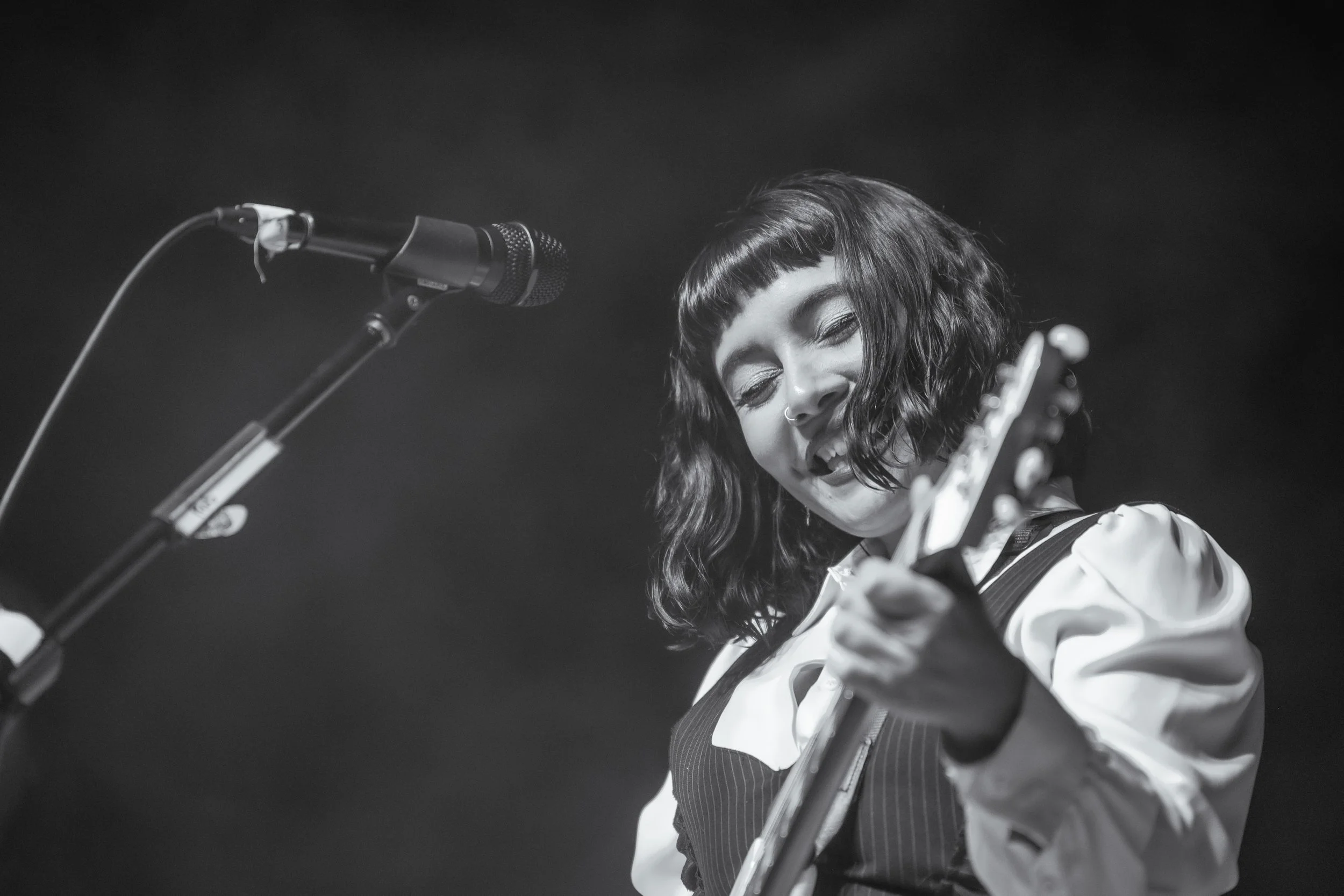 Guitarrista de cabello corto junto al micrófono, en blanco y negro.