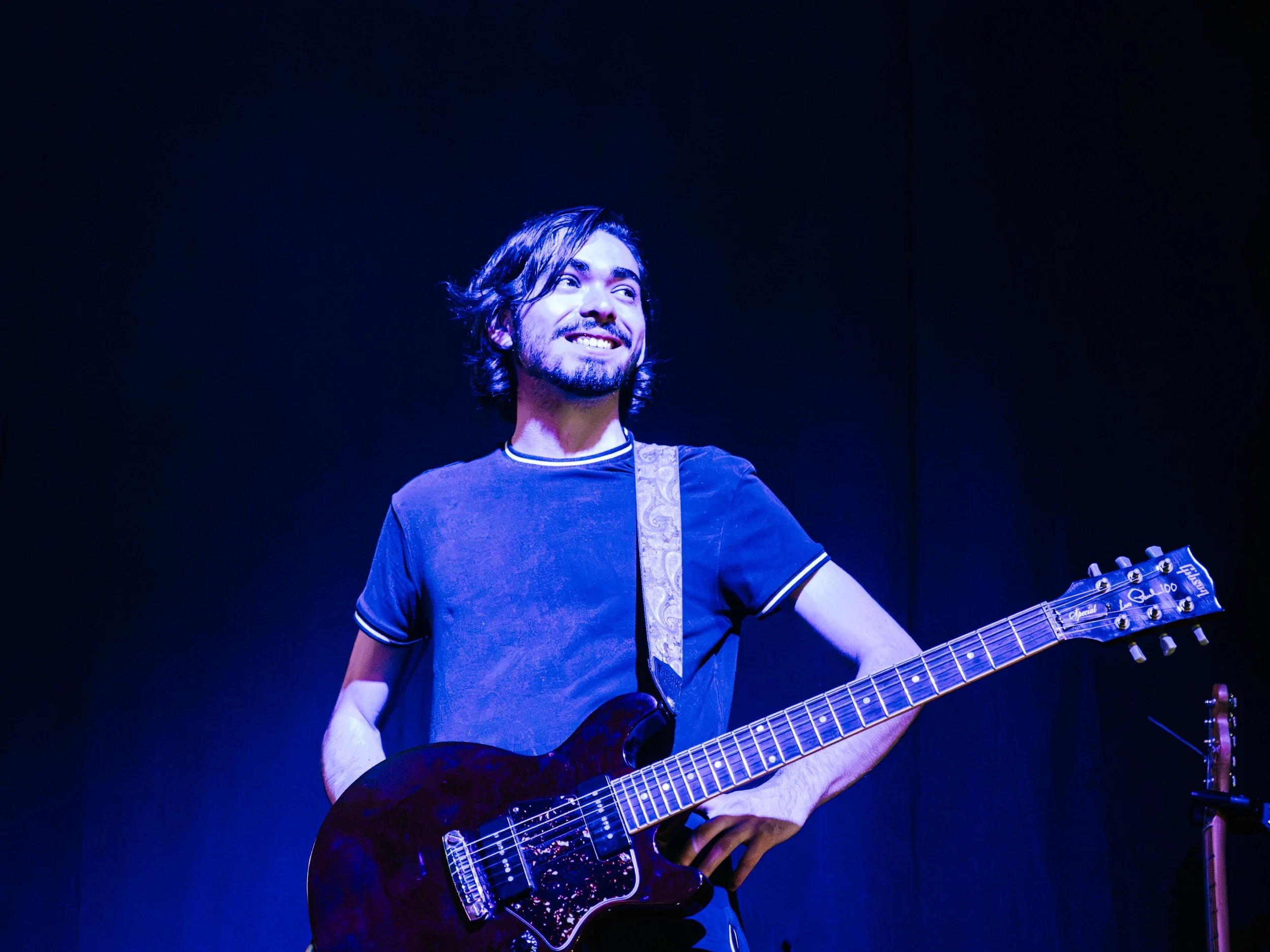 Guitarrista sonriendo bajo iluminación azul.
