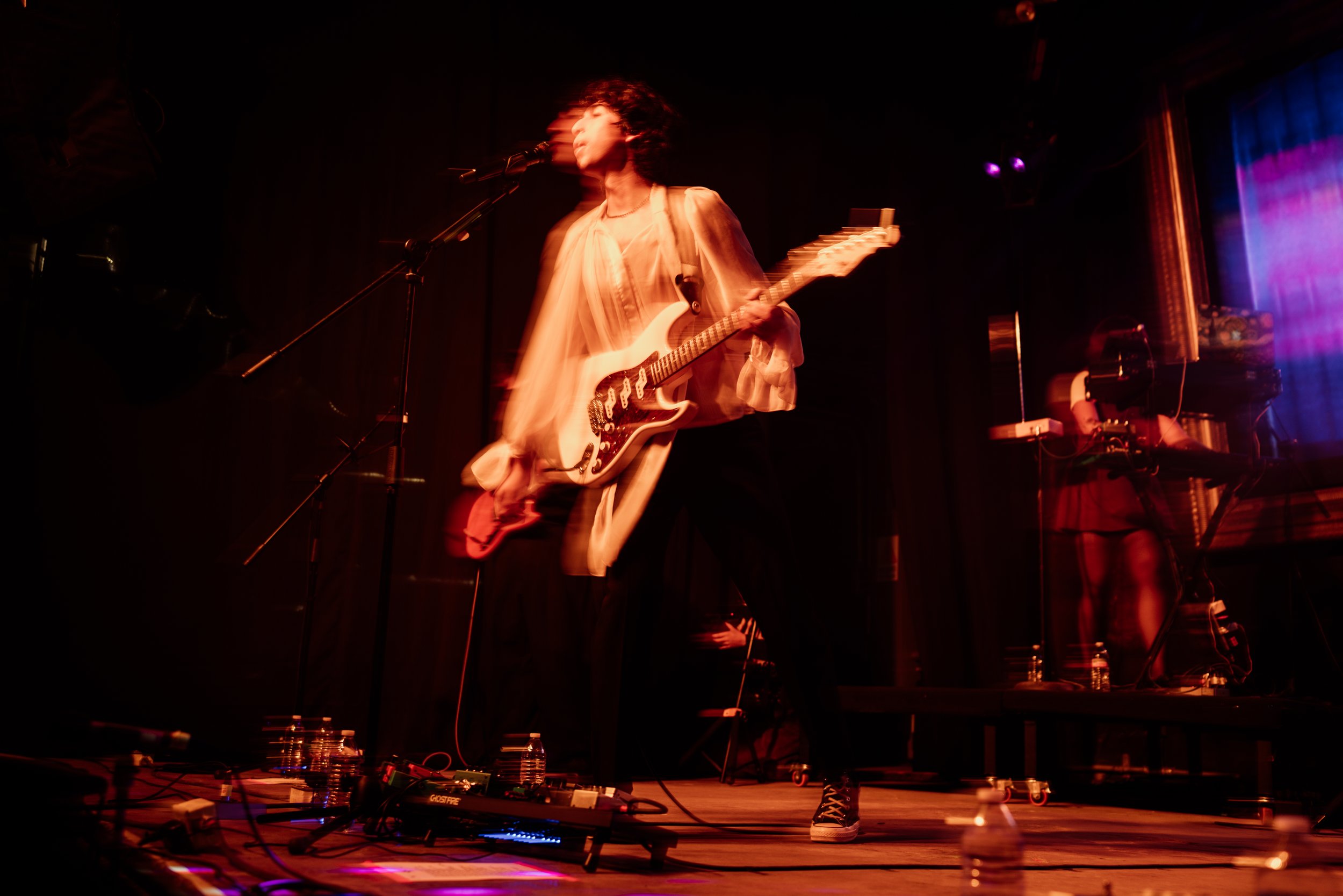Guitarrista saltando sobre el escenario bajo luces rojas.
