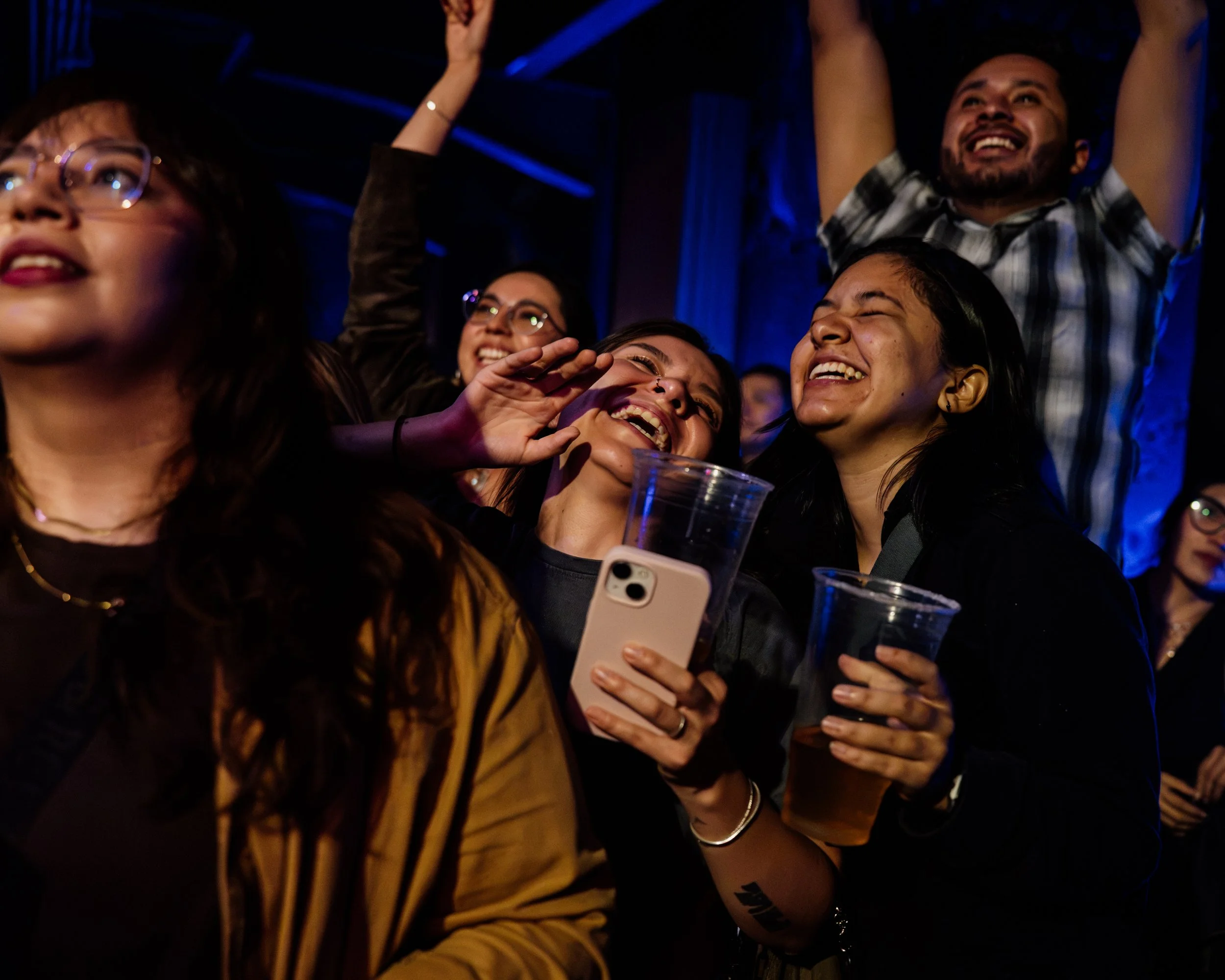 Asistentes sonriendo y levantando sus teléfonos durante un concierto.
