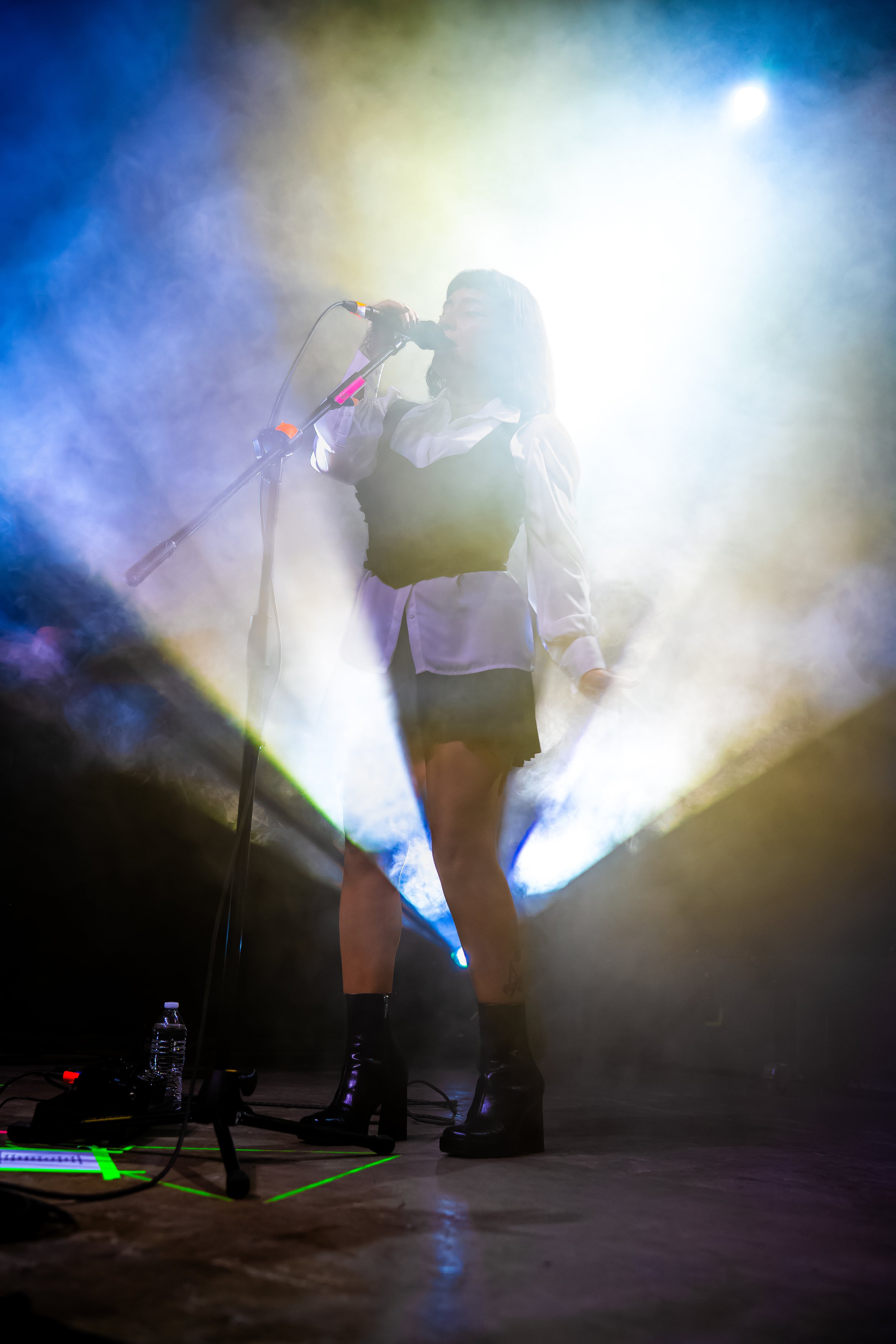 Cantante a contraluz rodeada de haces de luz azul y blanca.