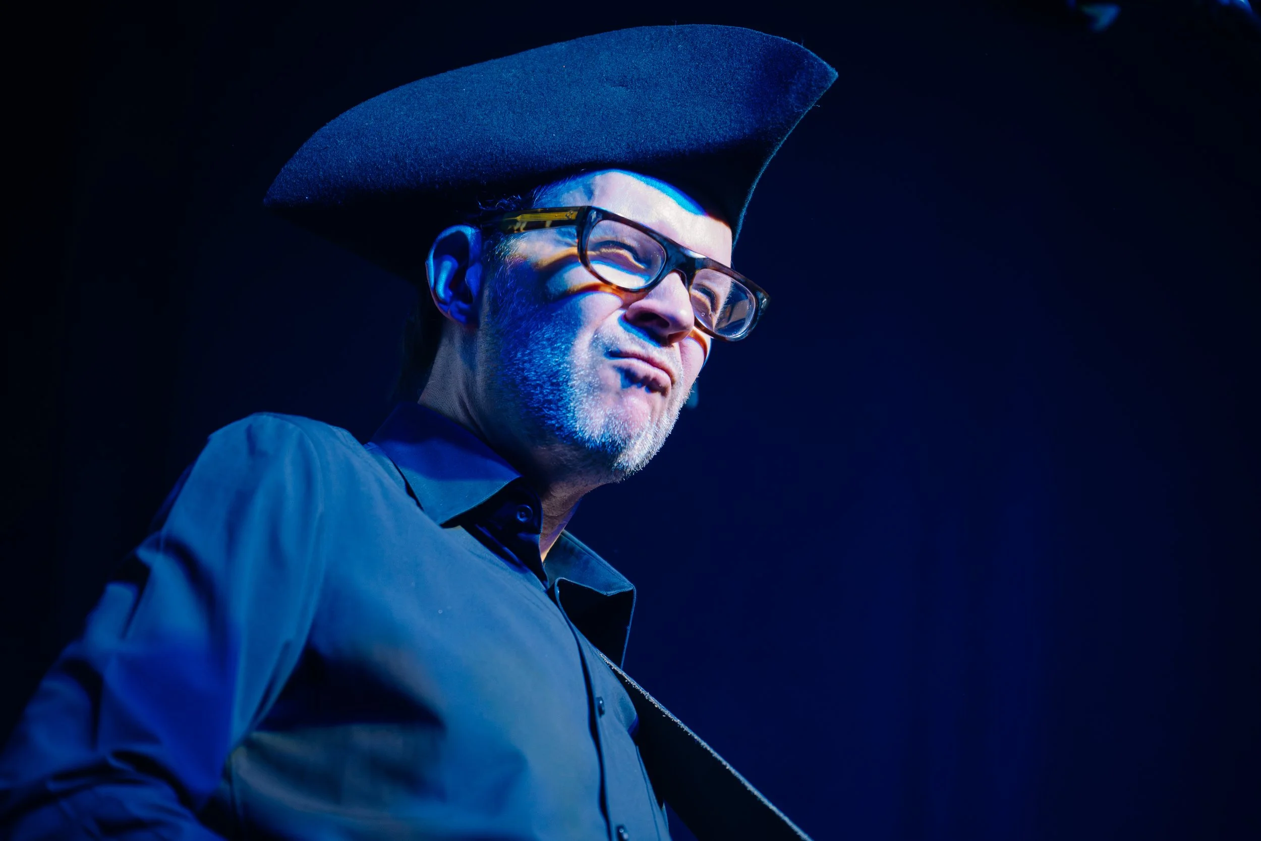 Músico con sombrero y lentes bajo iluminación azul.