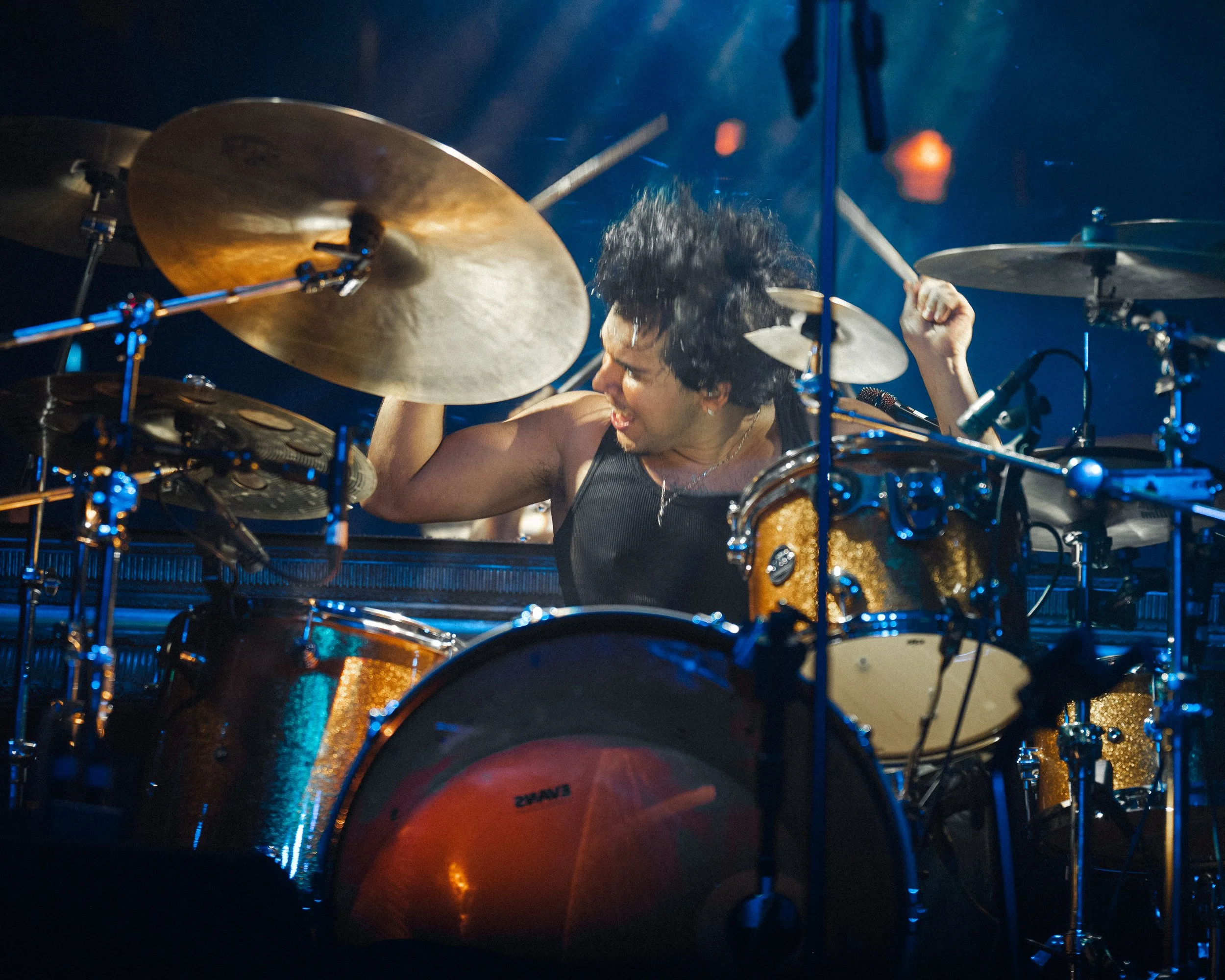Baterista tocando entre platillos y tambores durante un concierto.