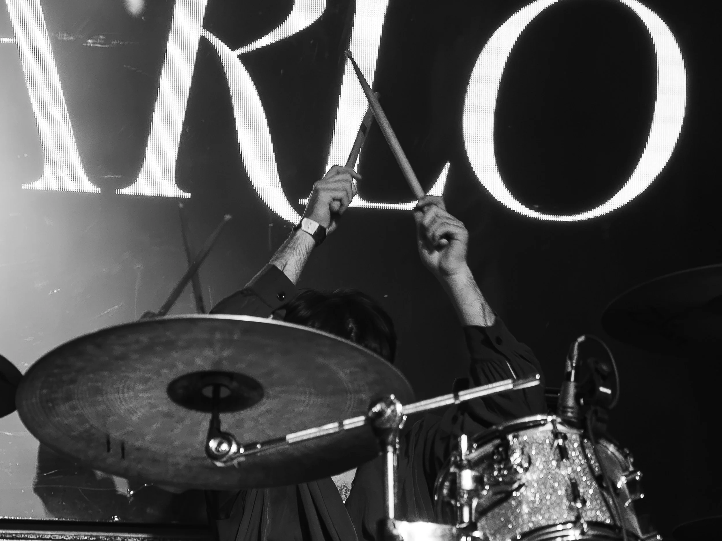 Baterista con las baquetas levantadas, en blanco y negro.