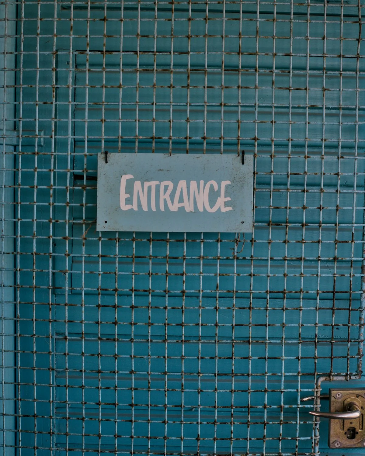 A blue metal gate with a white sign that says 'ENTRANCE' in pink lettering.
