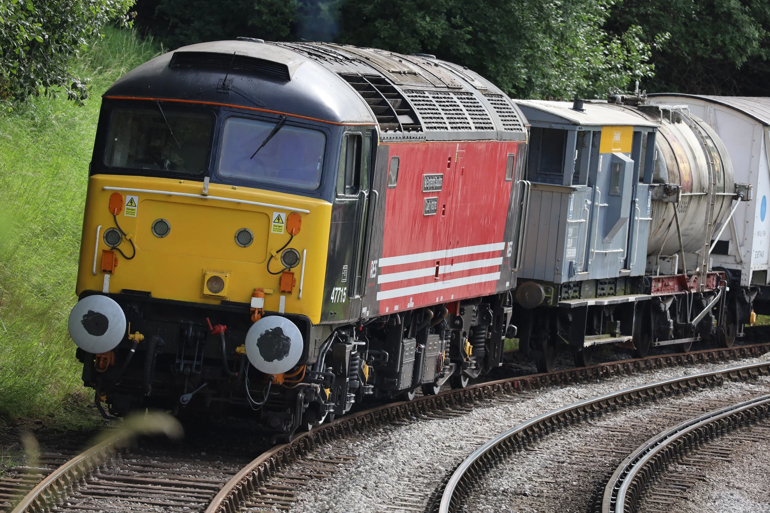 A diesel locomotive train moving along curved railroad tracks surrounded by green trees and grass.