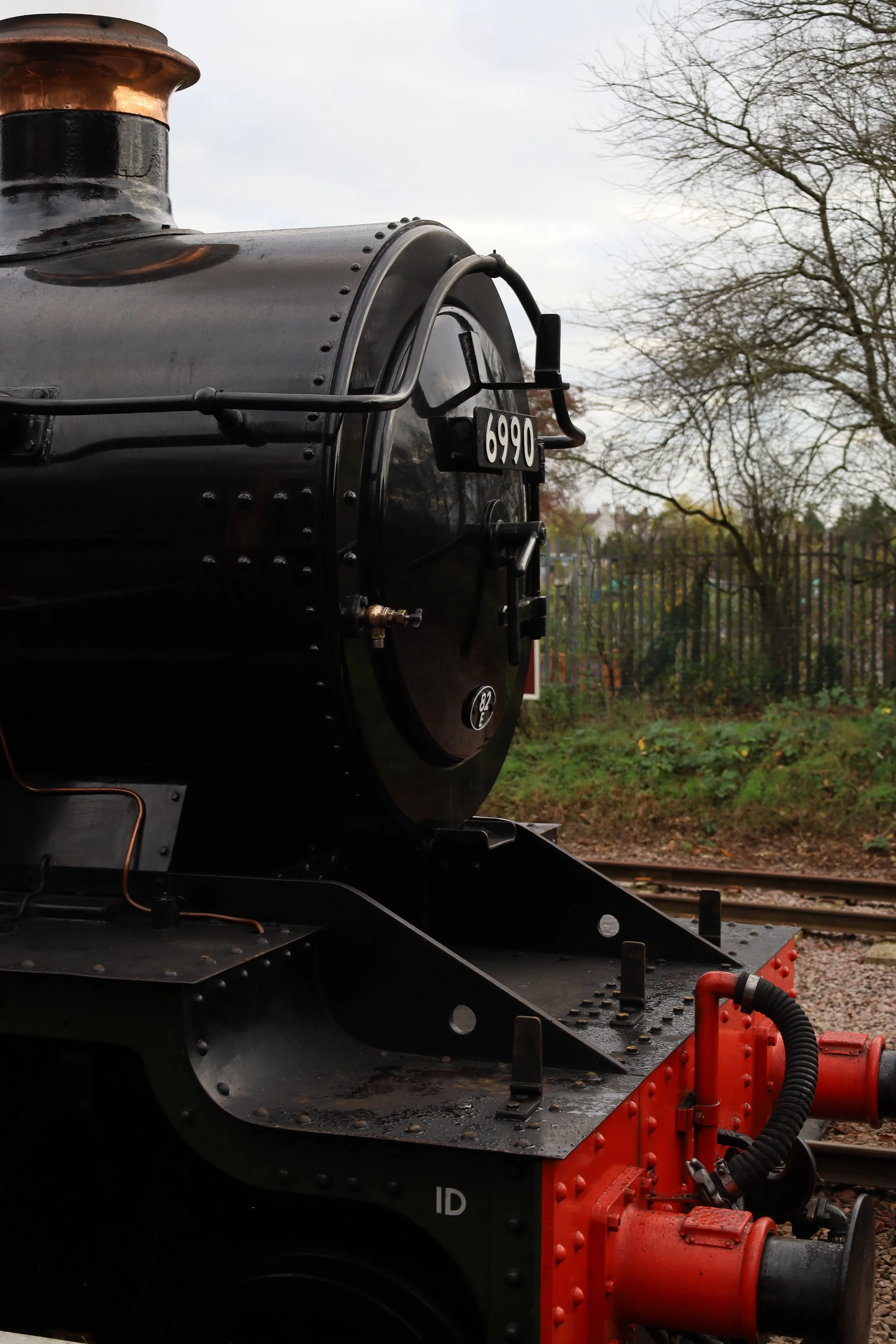 Close-up of the front part of a black steam locomotive with a red coupling device and part of the train track visible in the background.