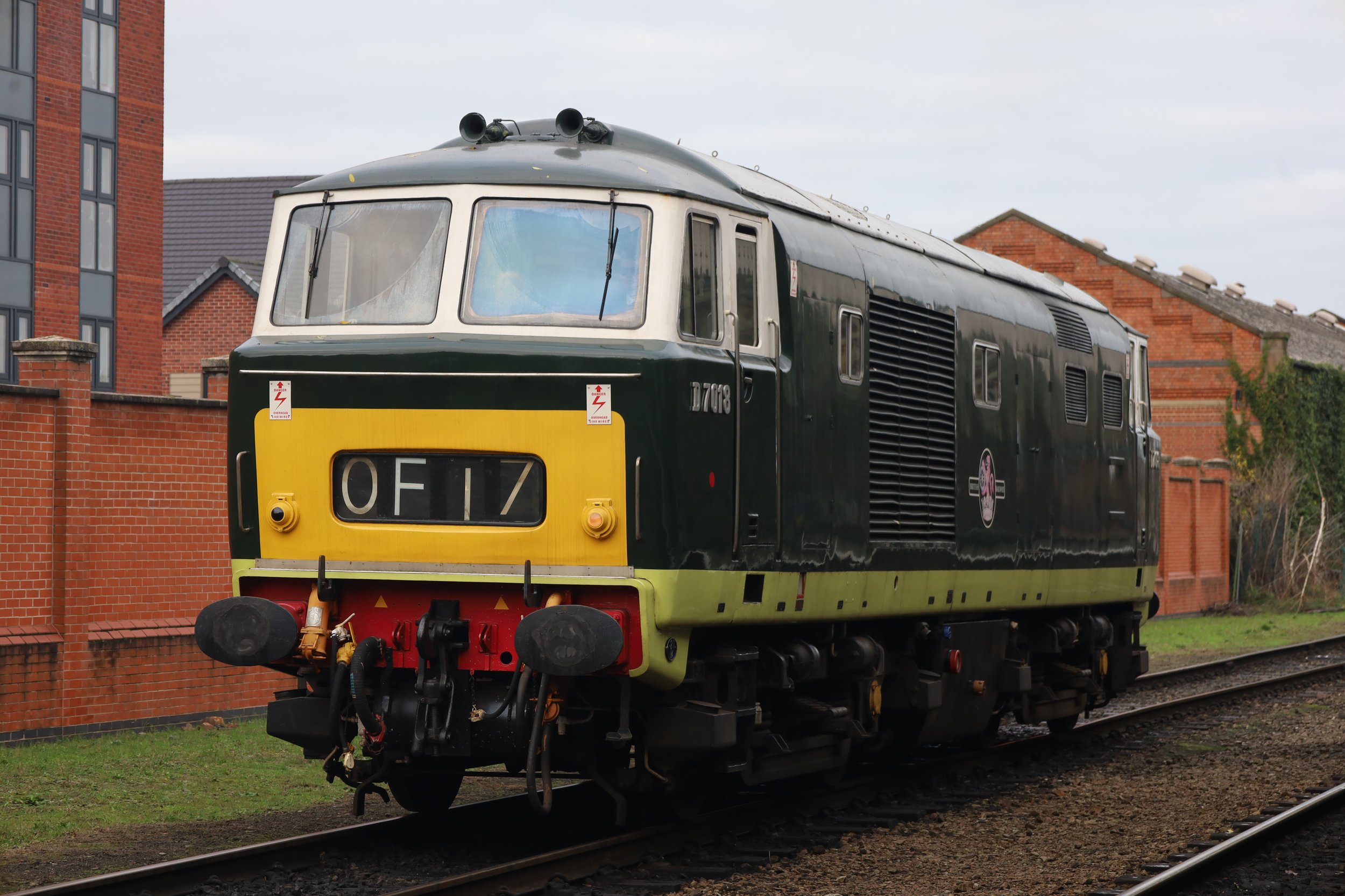 A vintage train engine with black and yellow paint is on train tracks in front of brick buildings.