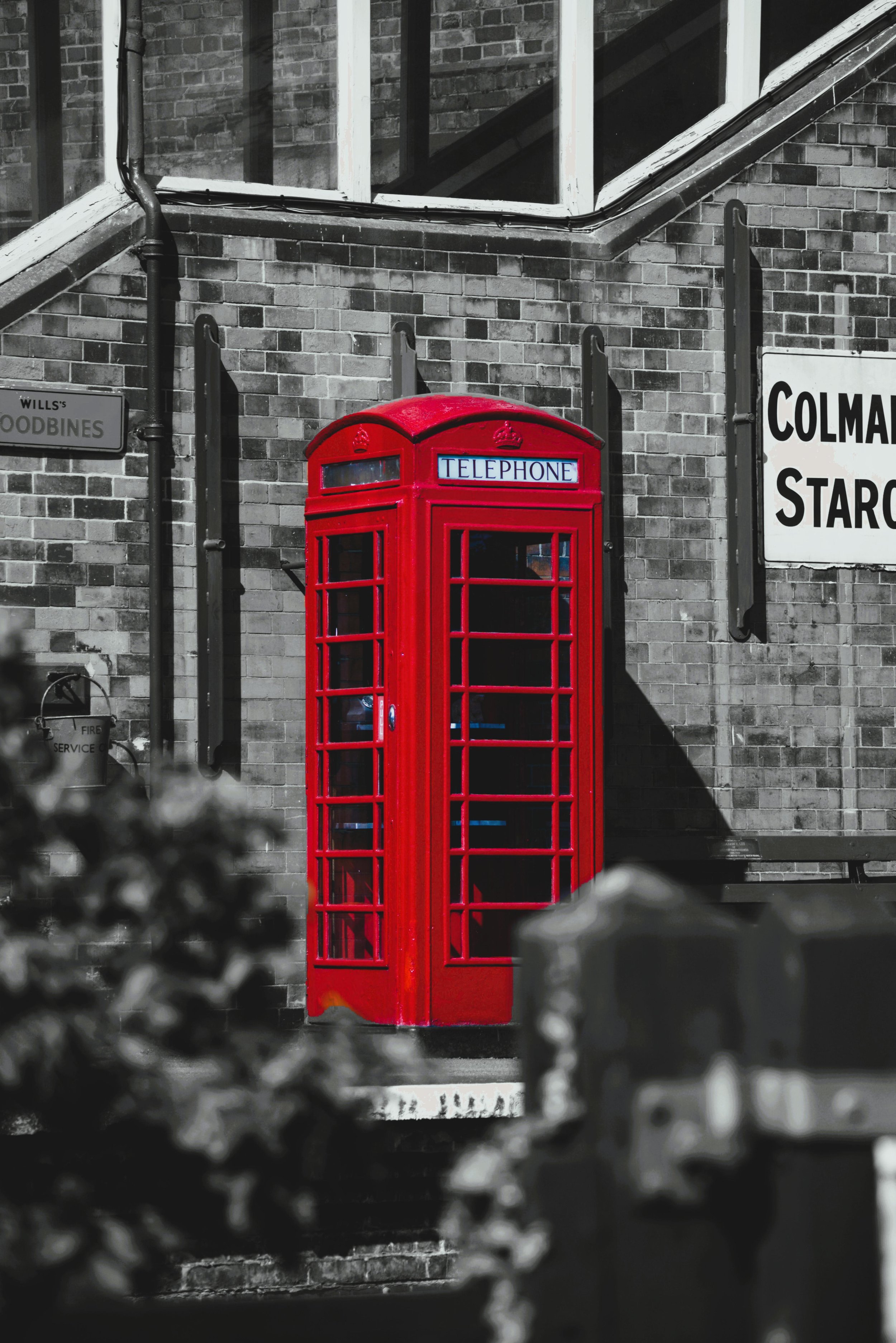 A bright red British telephone booth against a brick building with black and white background elements.
