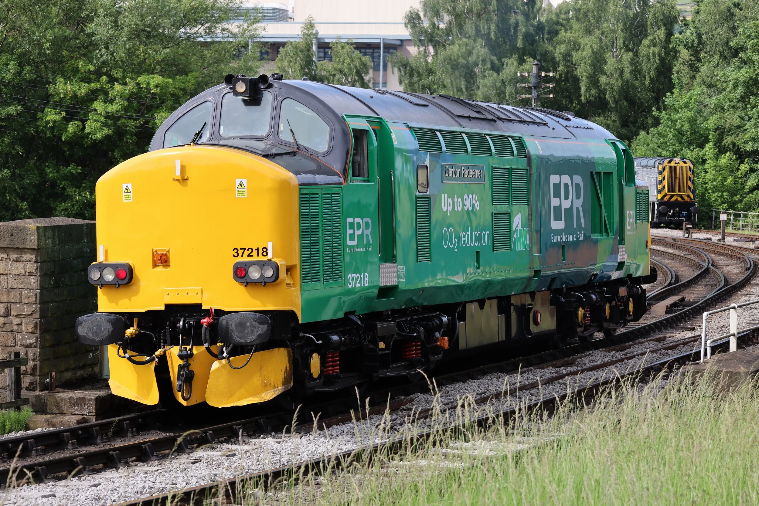A green and yellow train labeled Europhoenix Rail on a railway track surrounded by green trees.