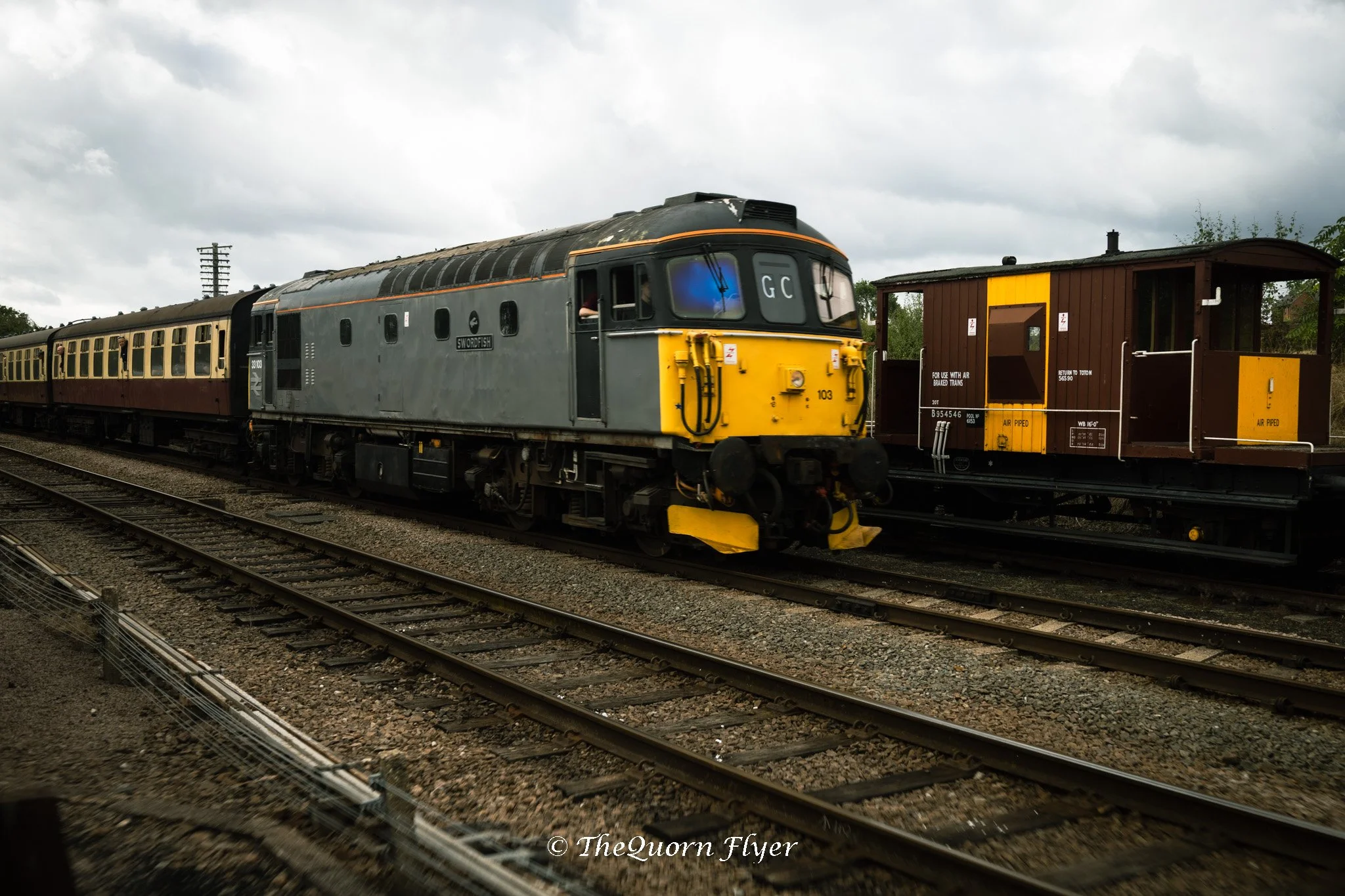 A train with a gray locomotive and vintage passenger cars on railway tracks under cloudy sky.