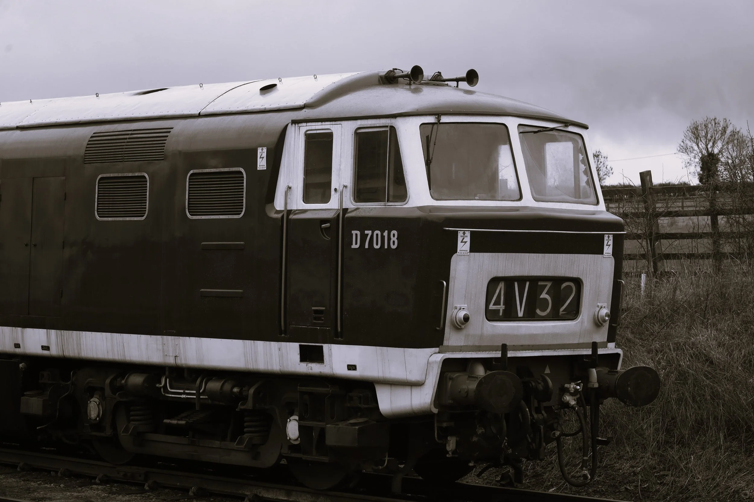 Black and white photo of an old train's front section, featuring a large windshield, two horns on the roof, and the number D7018 on the front.
