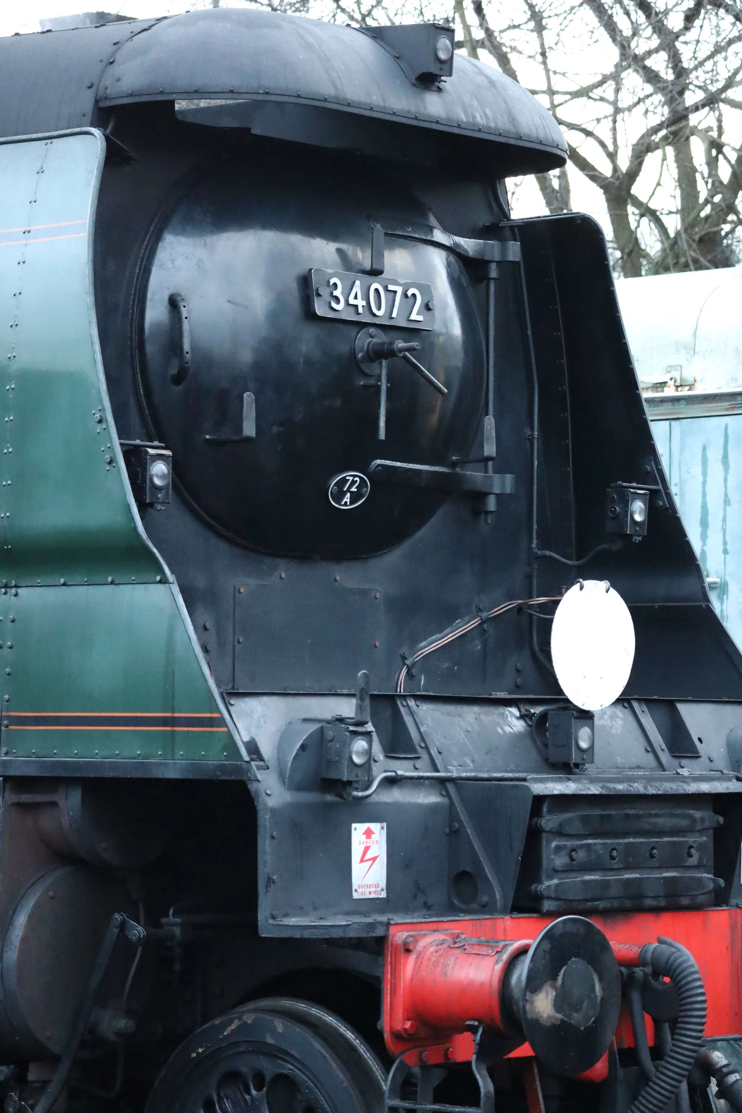 Close-up of the front of a vintage black steam locomotive with the number 34072 displayed on the front, and a warning sign for overhead live wires.