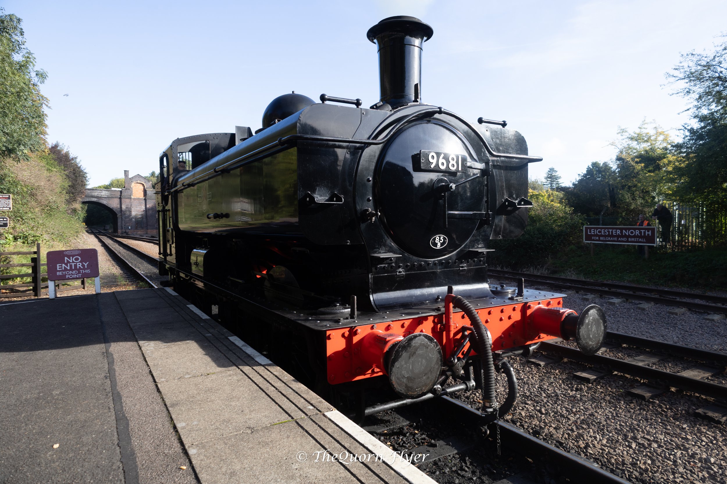 A vintage black steam locomotive with the number 968 on the front, on train tracks near a tunnel entrance, with trees and signs nearby and a clear sky overhead.