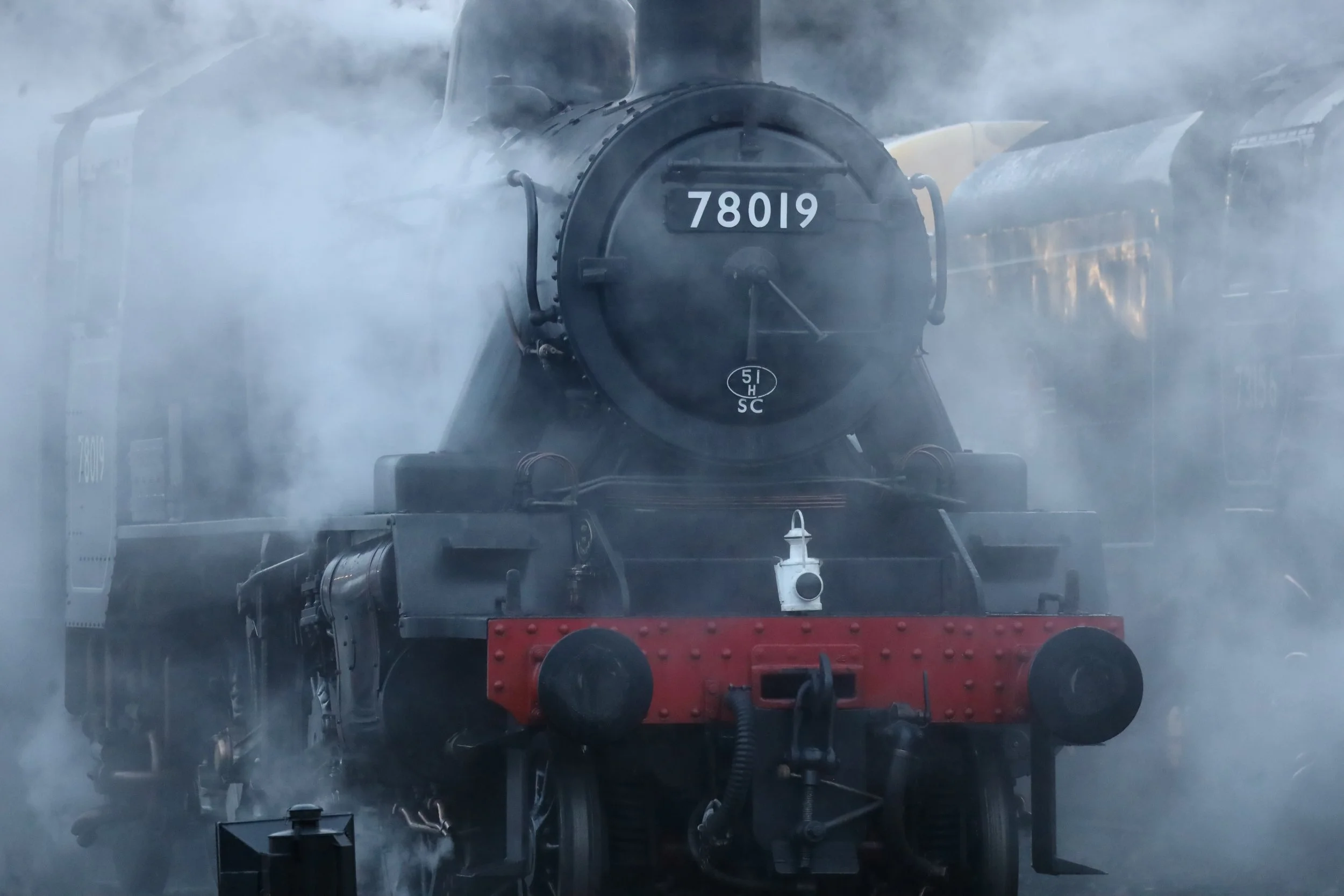 A steam locomotive train emerging from a tunnel with steam and smoke surrounding it.