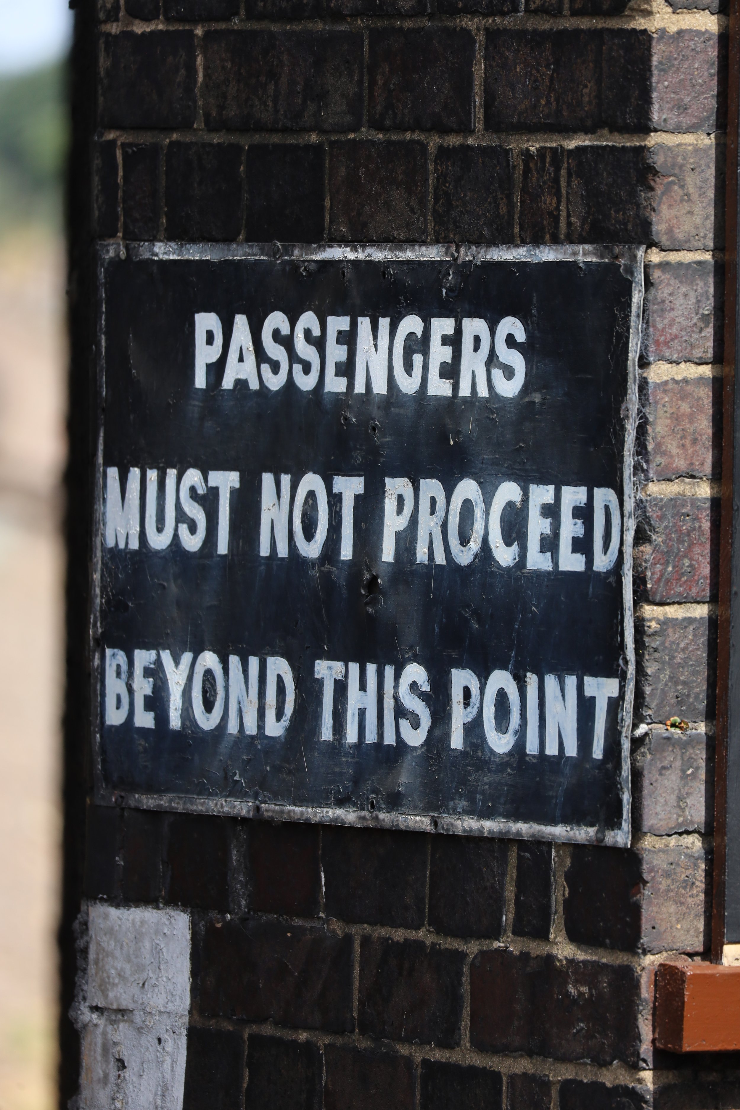 A black and white sign on a brick wall that reads: "Passengers must not proceed beyond this point".