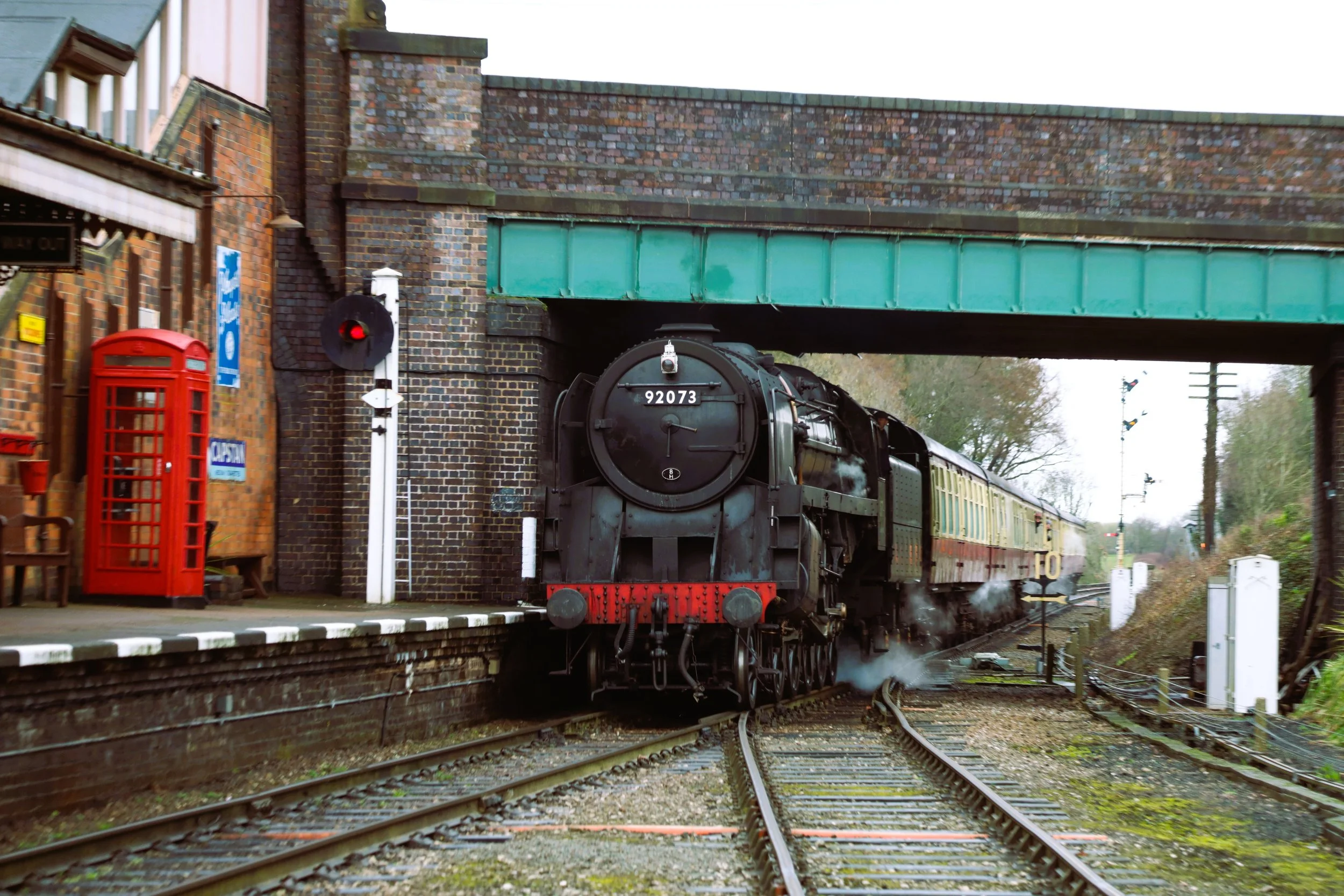A vintage steam train with the number 92073 traveling under a brick railway bridge.