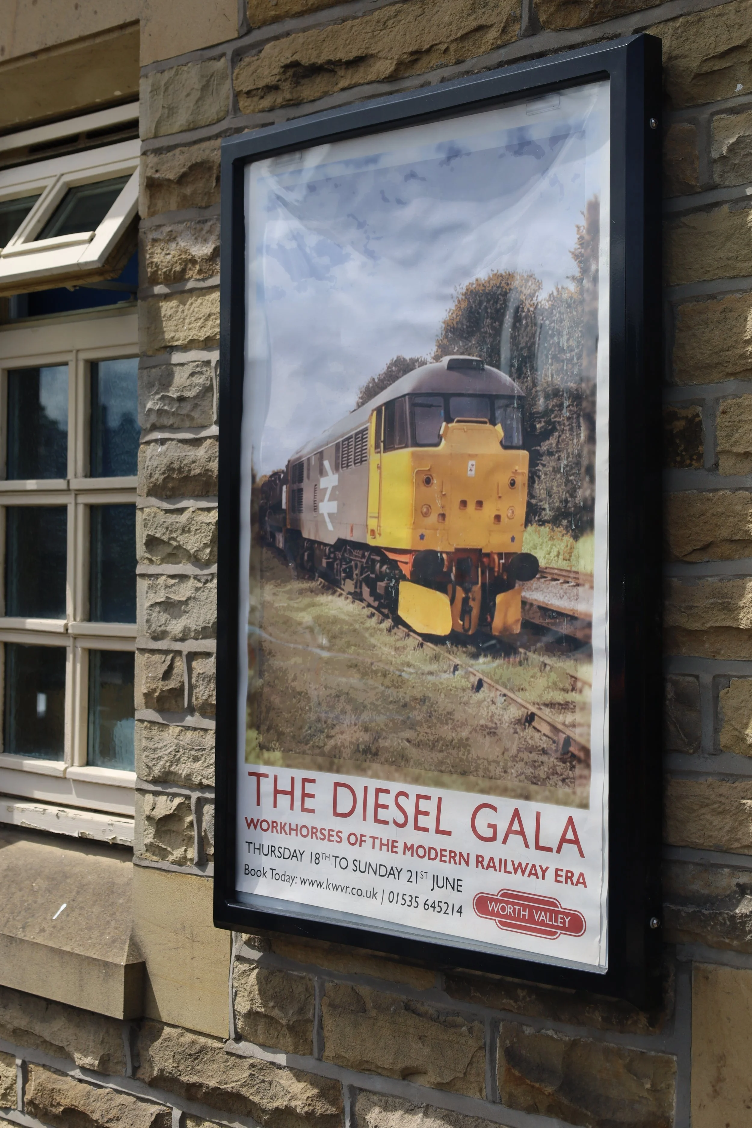 A poster on a brick wall advertising 'The Diesel Gala,' showcasing a vintage diesel train. The poster includes details about the event dates, booking information, and mentions the Worth Valley Railway.
