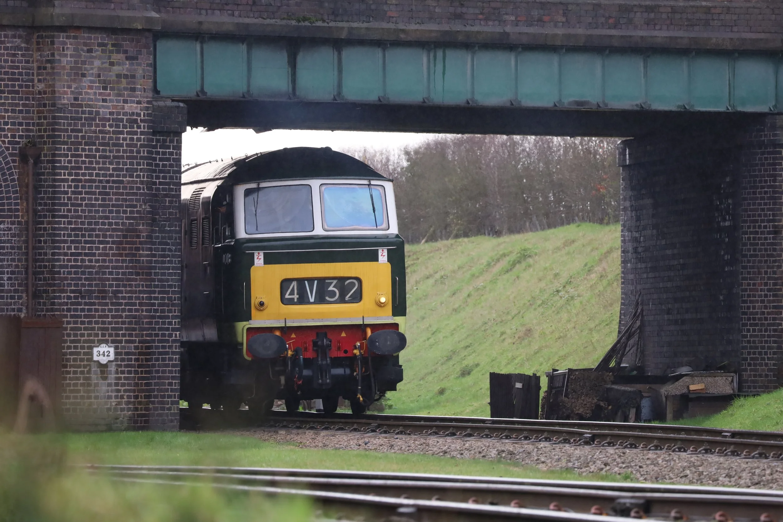 A vintage train emerging from a brick underpass, with green grass and trees in the background.