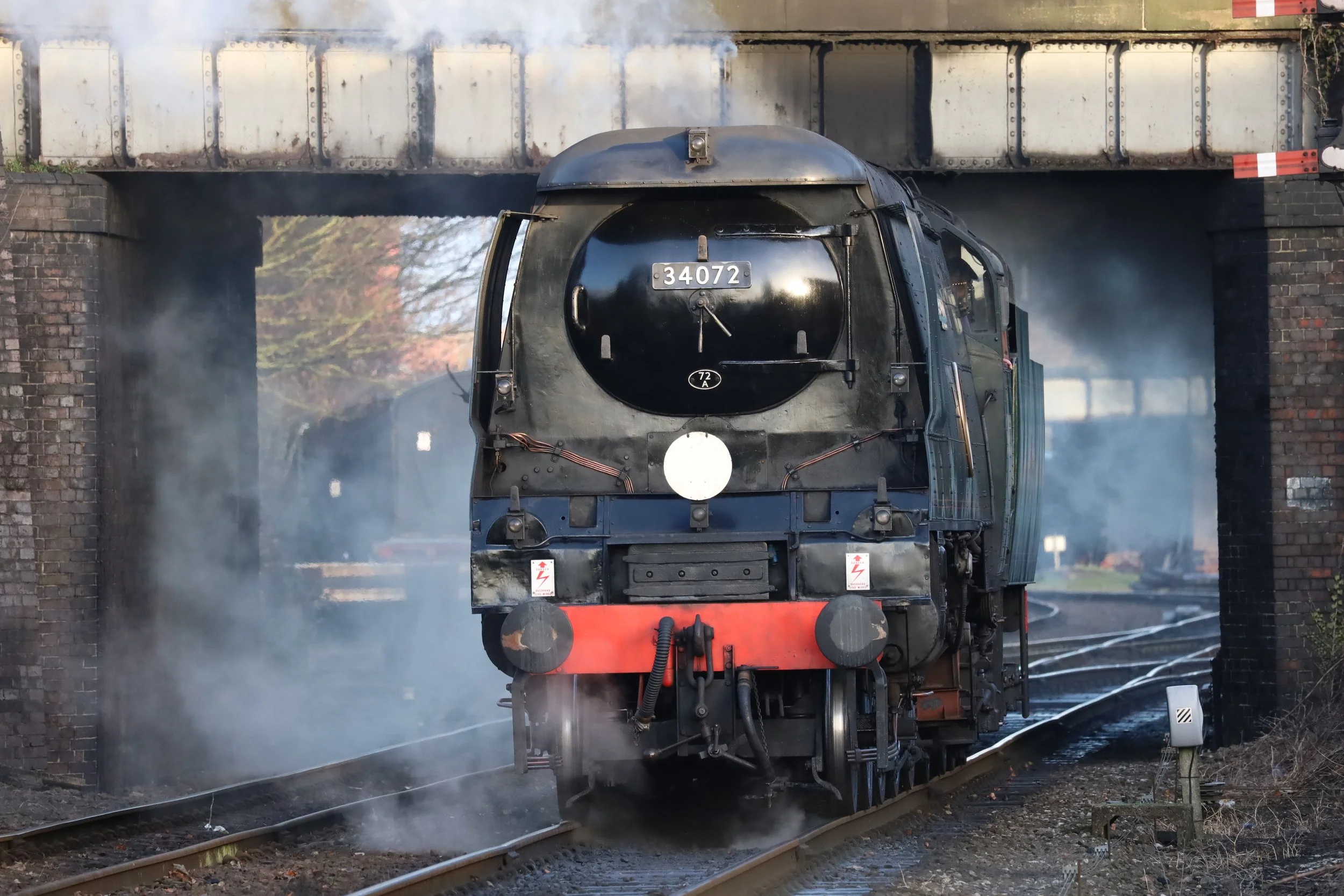 A black steam locomotive train moving through a bridge, emitting steam.