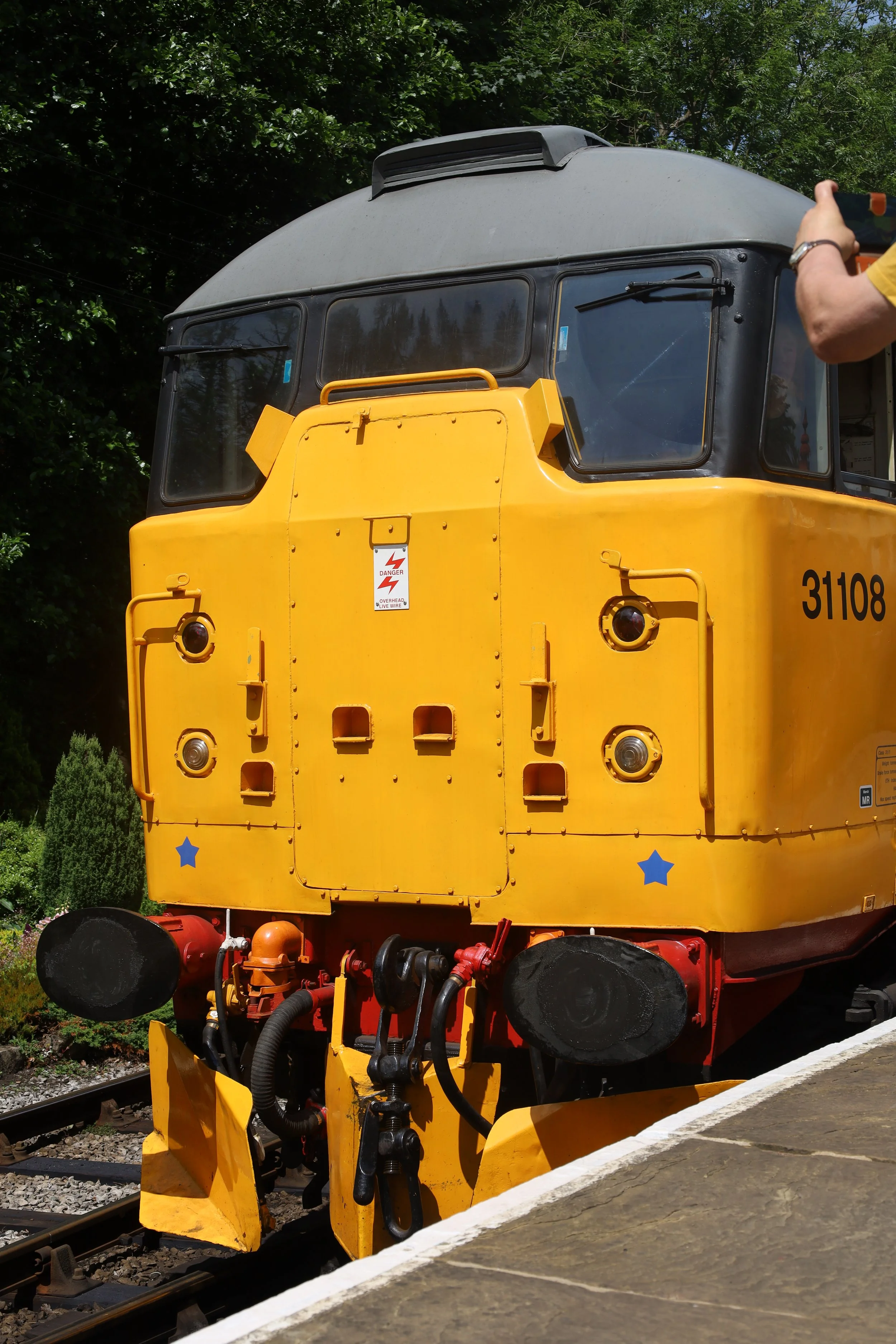 Close-up of a yellow and black train locomotive at a station with trees in the background
