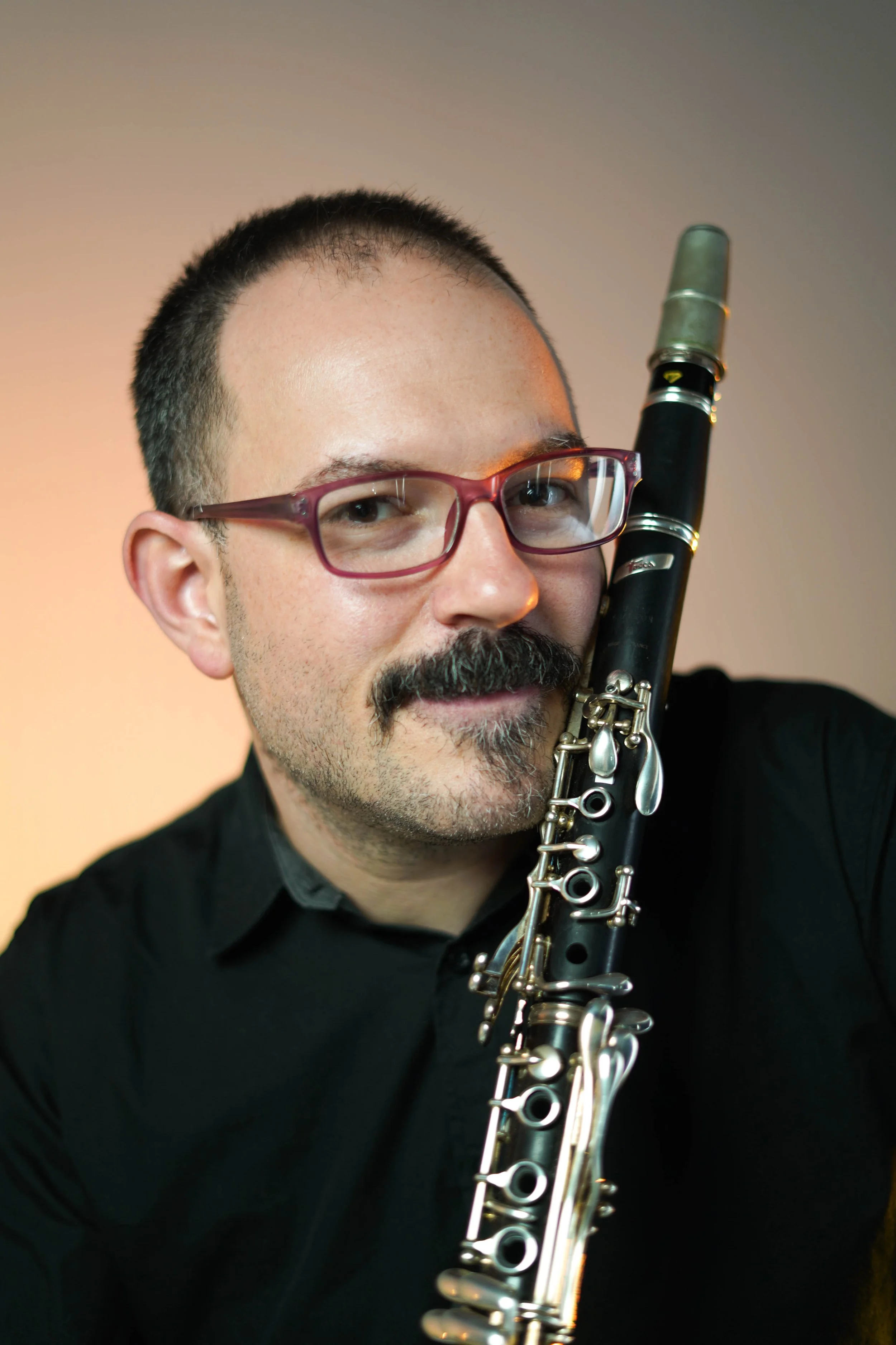 Close-up portrait of a man wearing red glasses and playing a black clarinet.