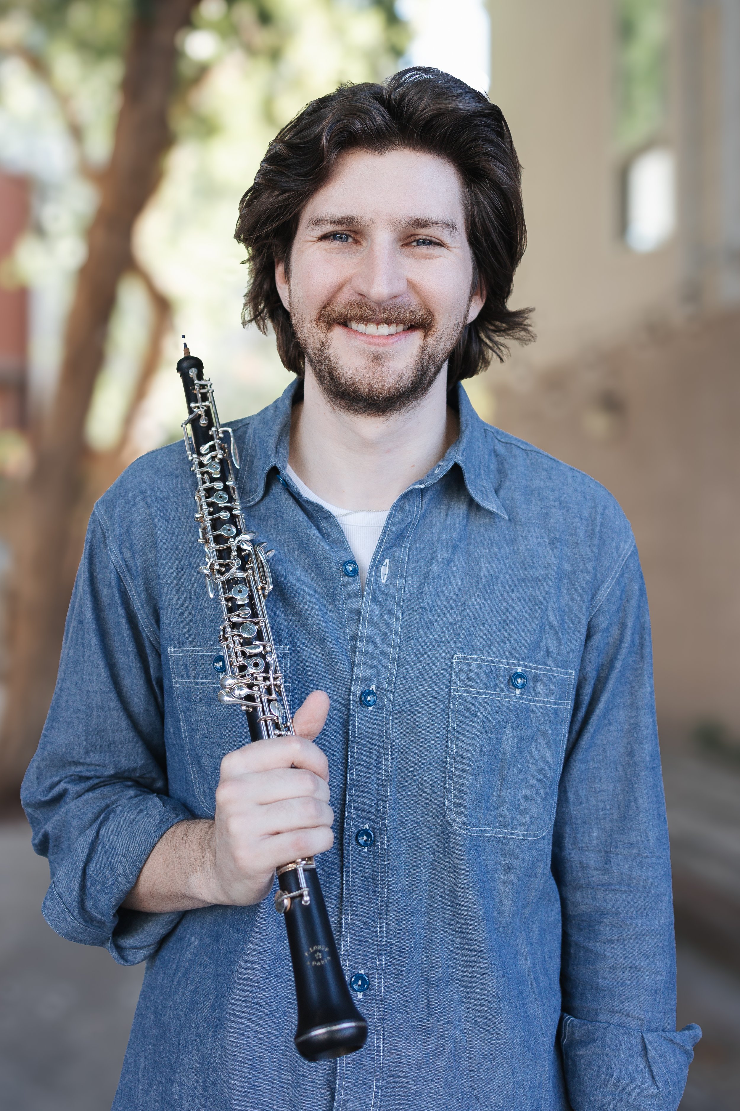 Smiling man holding a black oboe outdoors