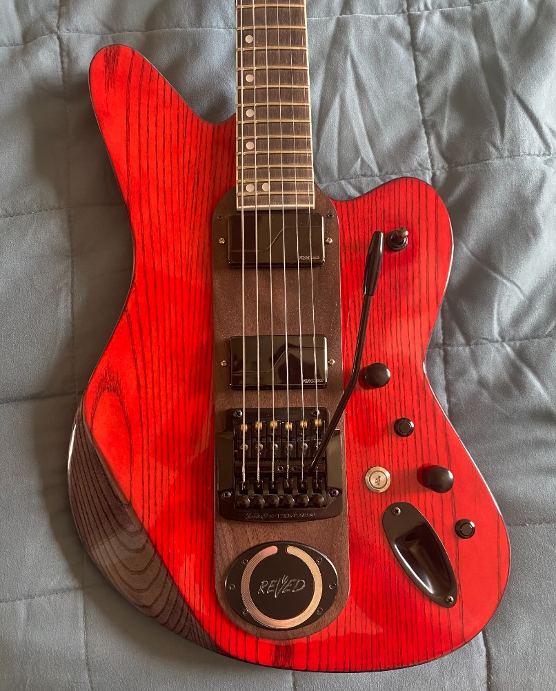Red electric guitar with a dark brown pickguard, multiple control knobs, a whammy bar, and a MagSafe compatible charging receiver.