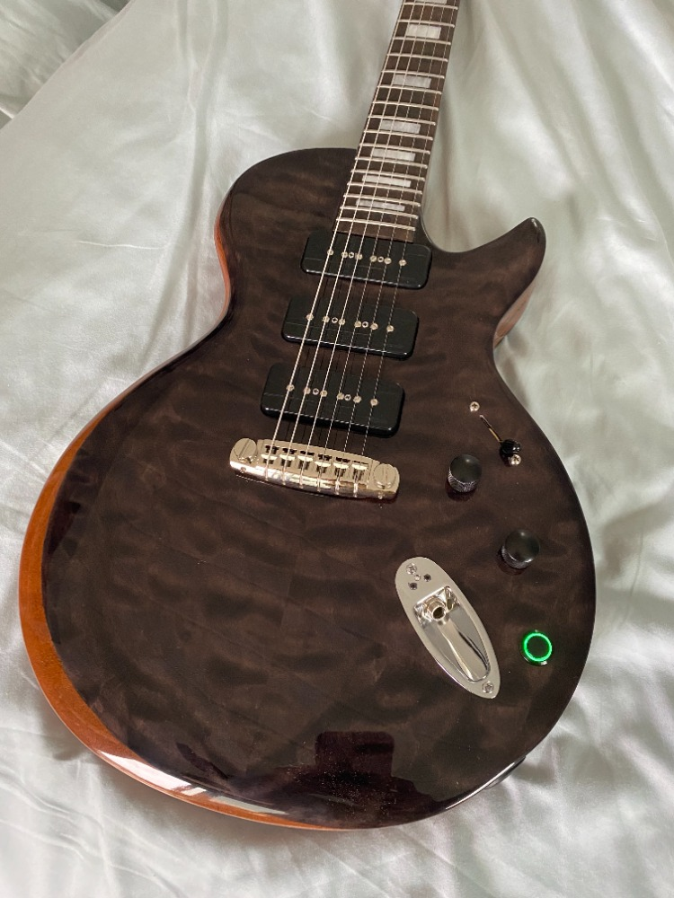 Dark brown electric guitar with three pickups, a bridge, and two control knobs, lying on a white surface.