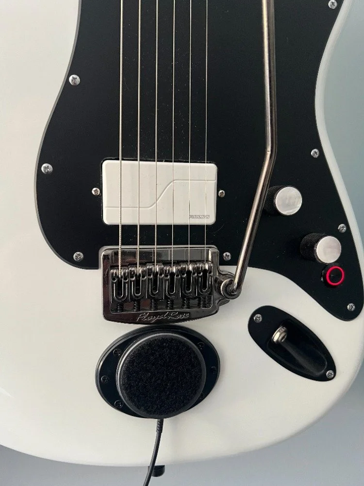 Close-up of an electric bass guitar with a pickguard, bridge, and control knobs. Magnetically mounted on the body is a black MagSafe charger, connected by a cord.
